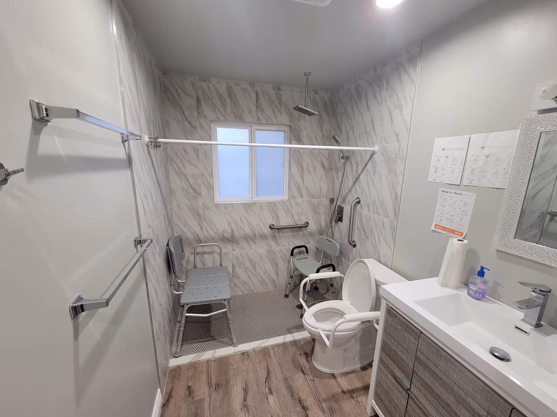 Accessible bathroom with tiled walk-in shower, grab bars, a bench, toilet, and sink.
