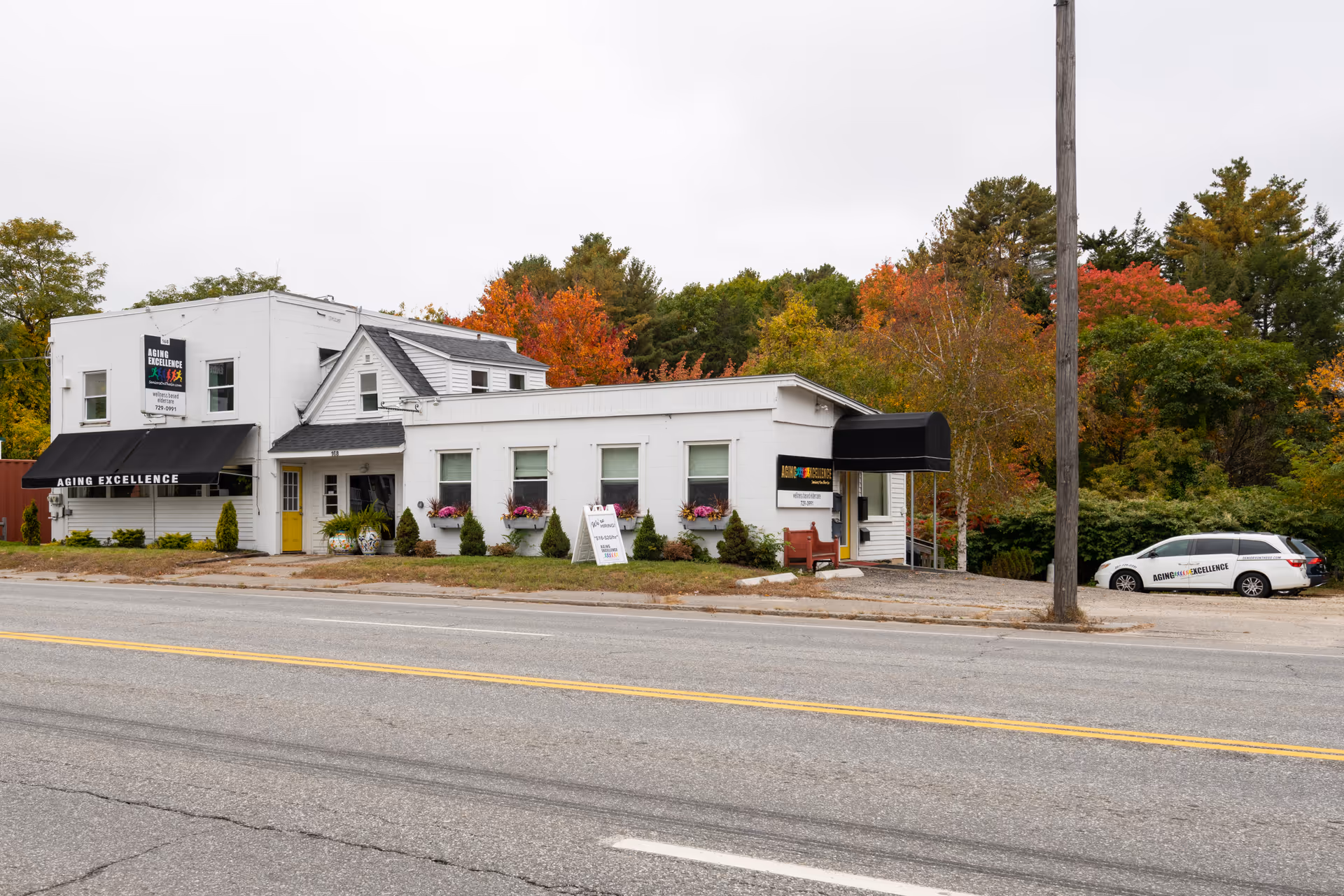 Exterior view of Aging Excellence senior living building with white facade and fall trees.