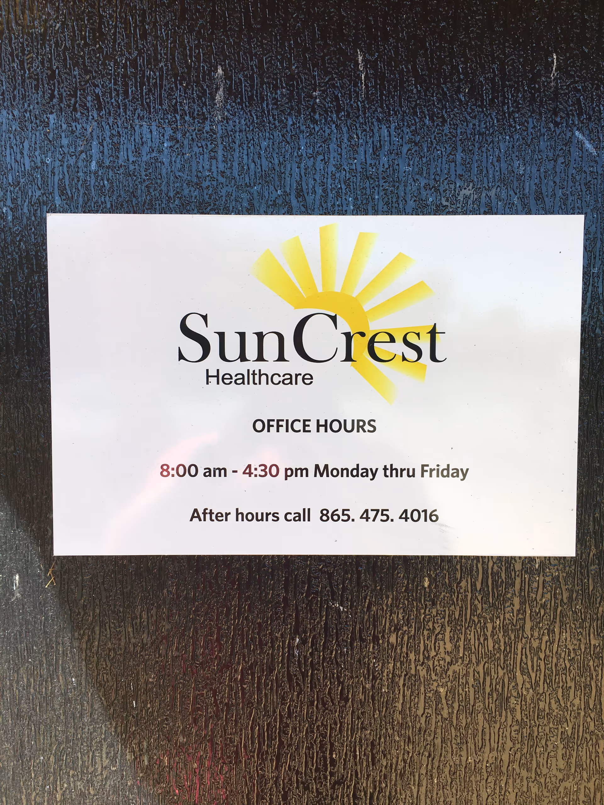 Sign on a dark exterior wall showing SunCrest Healthcare office hours.