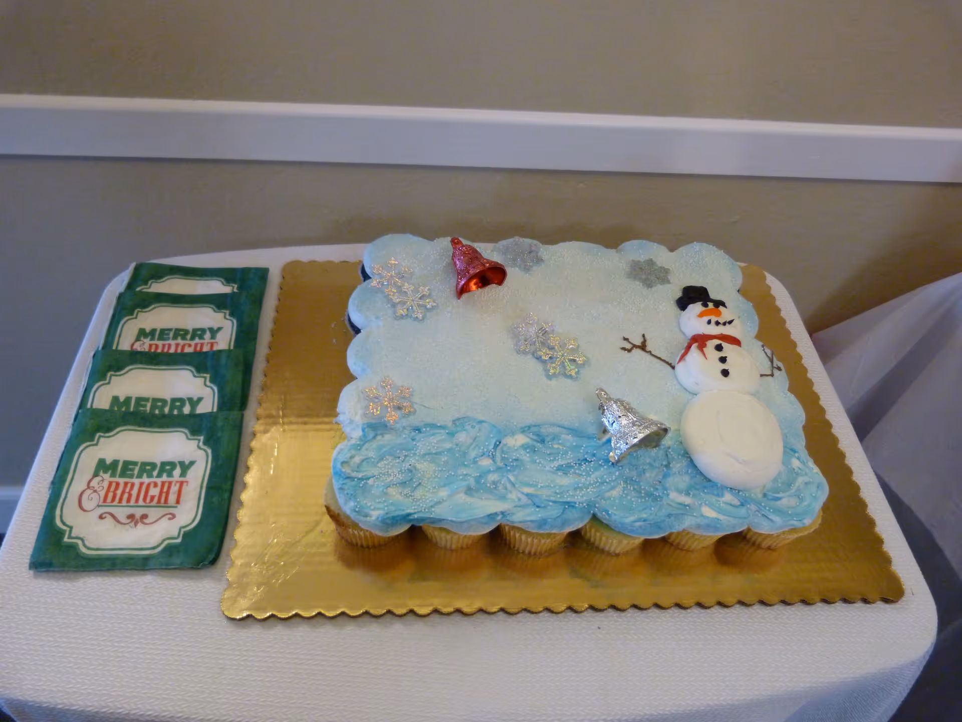 Winter-themed cake with snowman and snow decorations on a table beside Merry & Bright napkins.