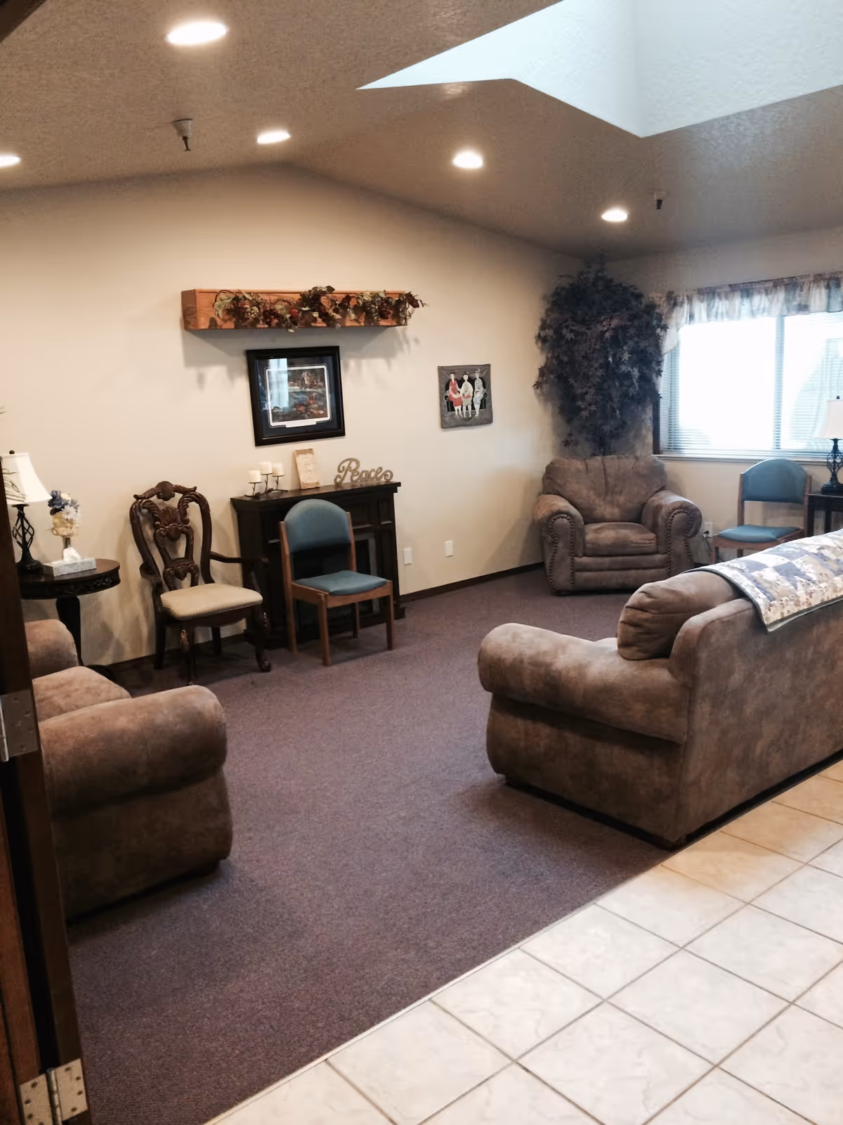A furnished common living room with upholstered sofas and armchairs, decorative wall art, and a carpeted floor.