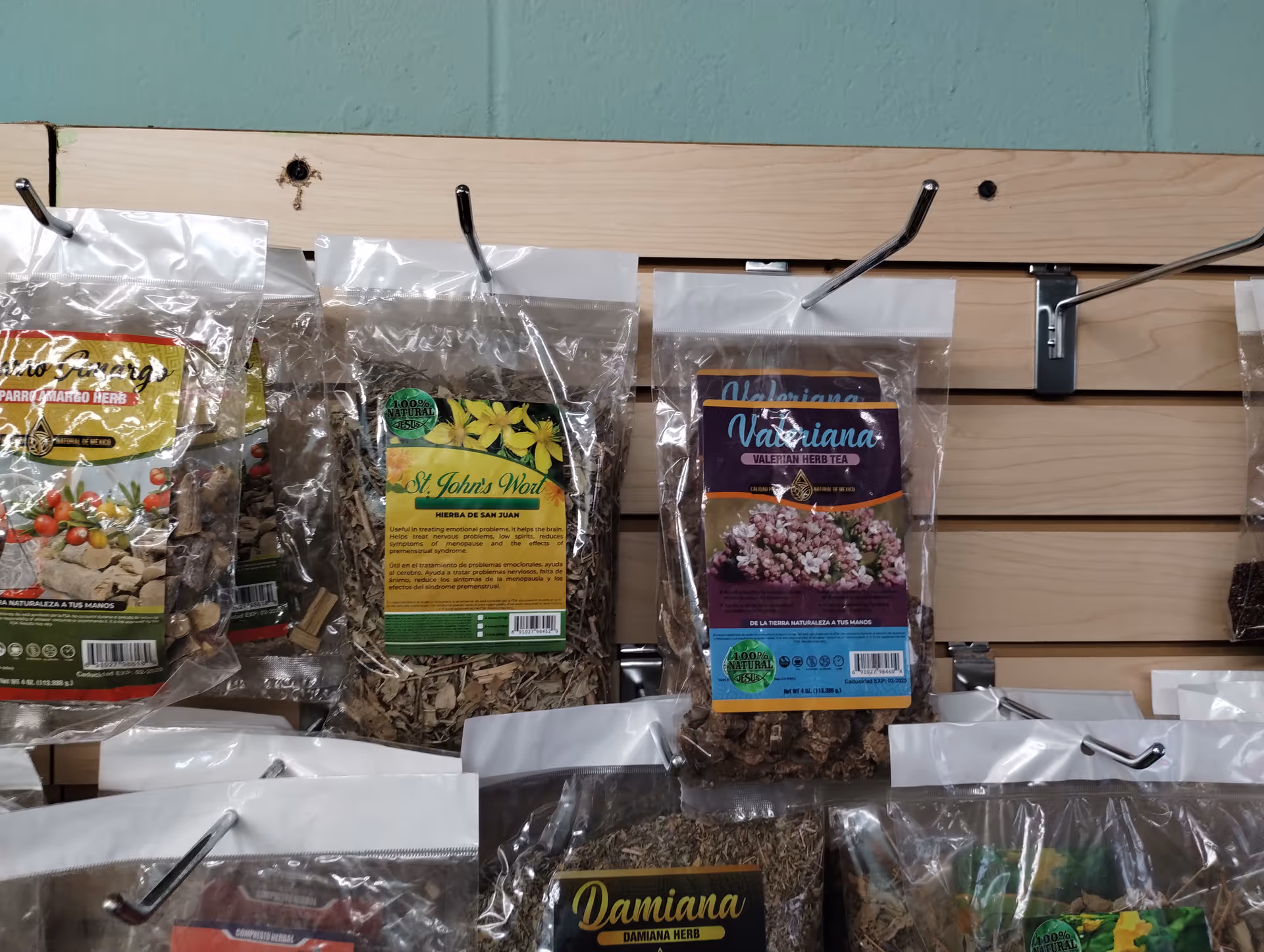 Assorted dried herbs in labeled plastic bags on a wooden display rack.