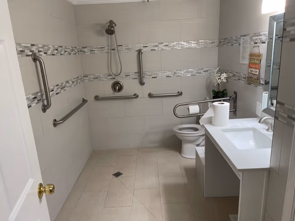 Accessible bathroom with multiple grab bars, a toilet, sink, and vanity.