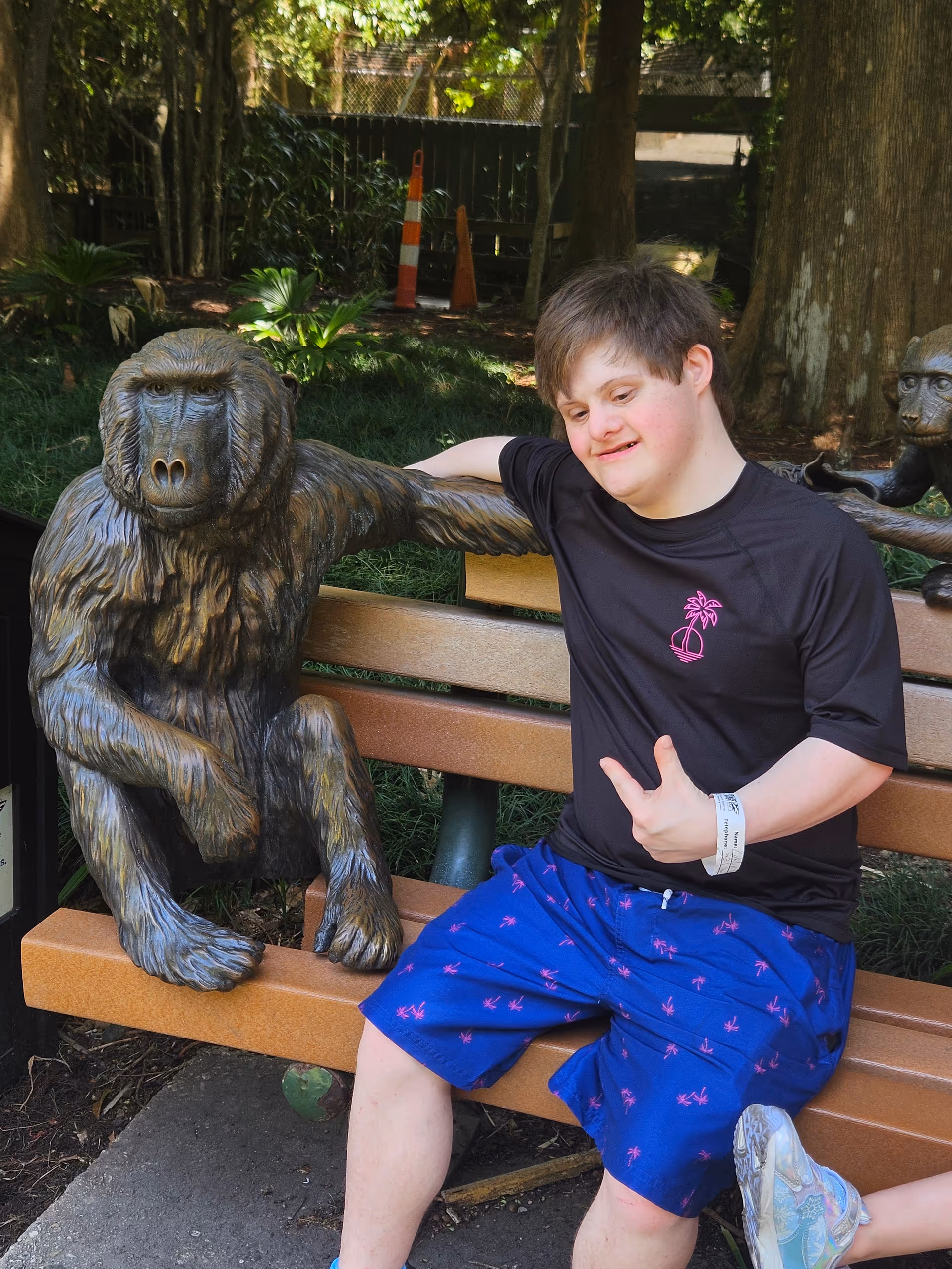 A person sits on a park bench beside a large monkey statue outdoors.