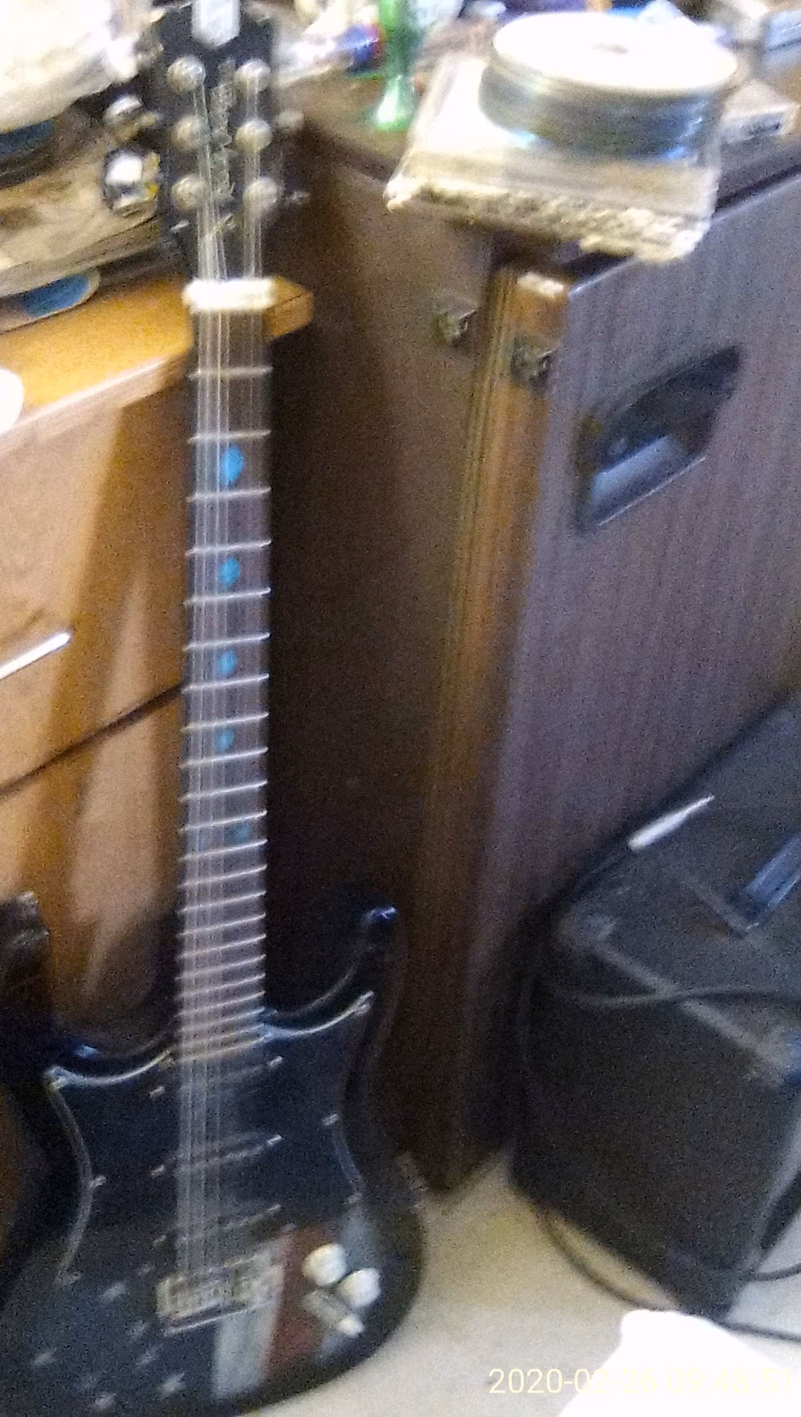 An electric guitar leaning against a wooden cabinet in a cluttered interior.