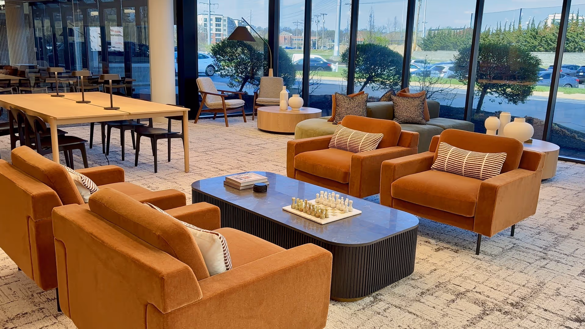 Warm, modern lounge area with orange seats, glass walls, and a chessboard on a coffee table.