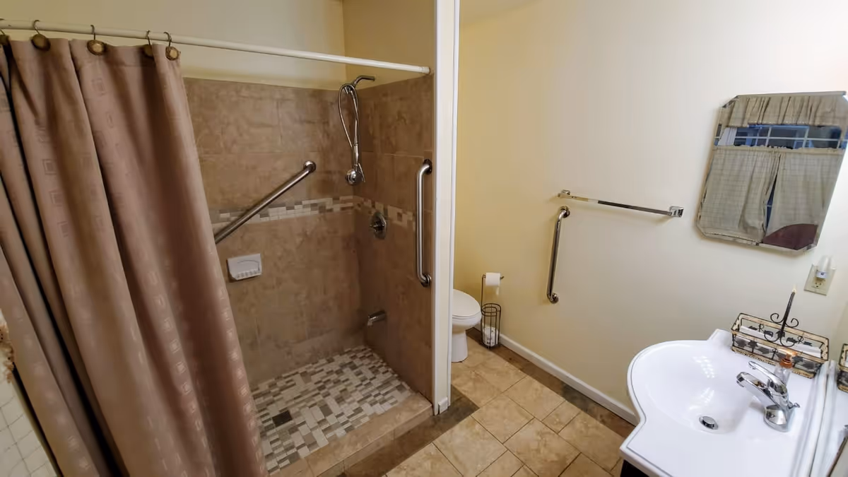 Accessible bathroom with shower, grab bars, toilet, and sink.