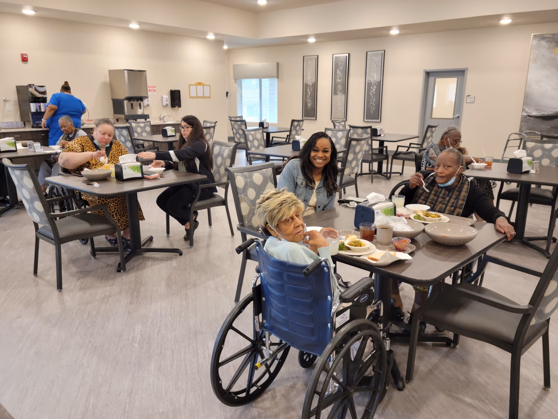 Residents and staff share a meal in a bright senior living facility dining room.