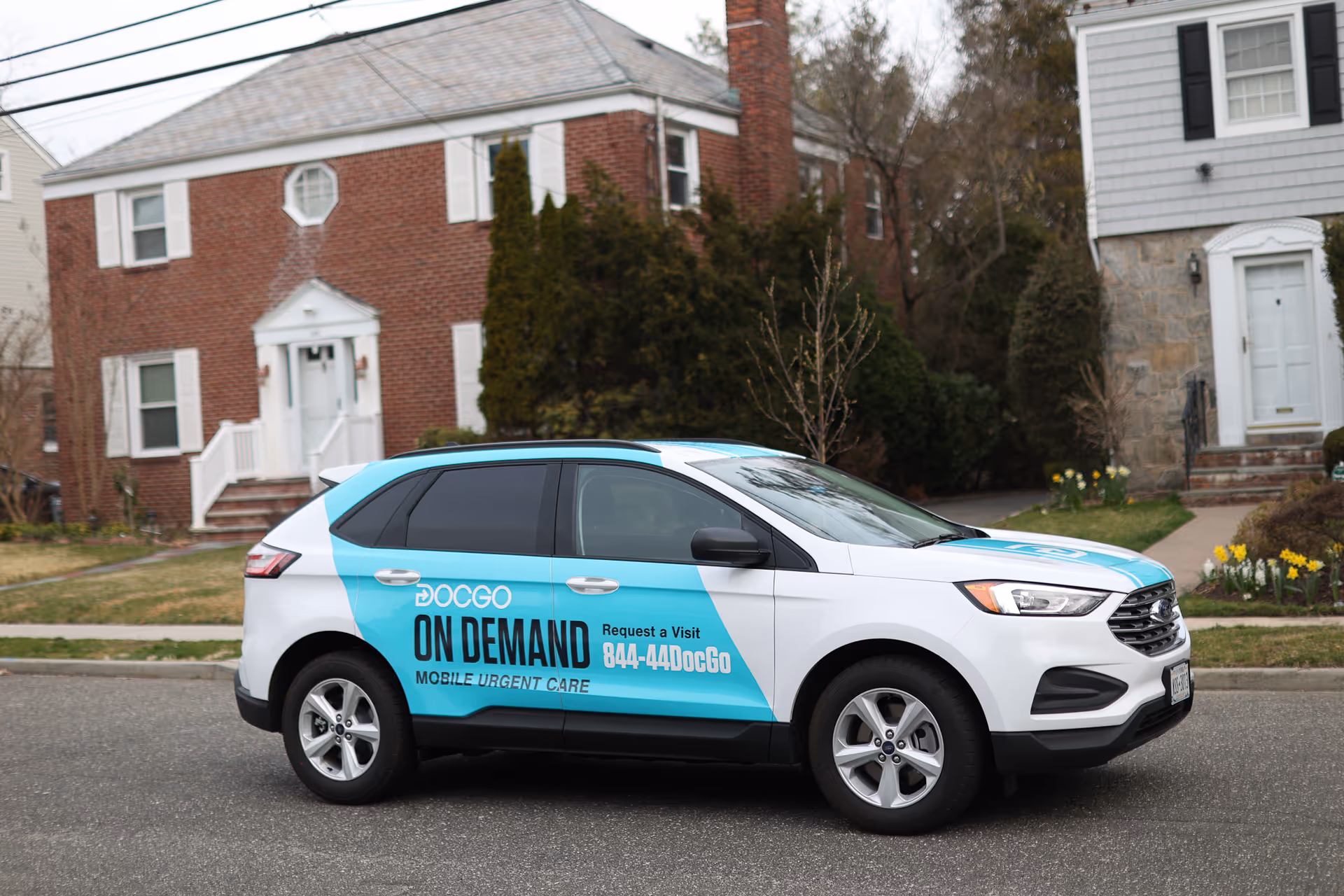DocGo mobile urgent care SUV with teal branding parked outside residential houses.