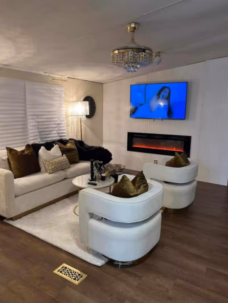 Modern senior living lounge with white furniture, fireplace, and wall-mounted TV.