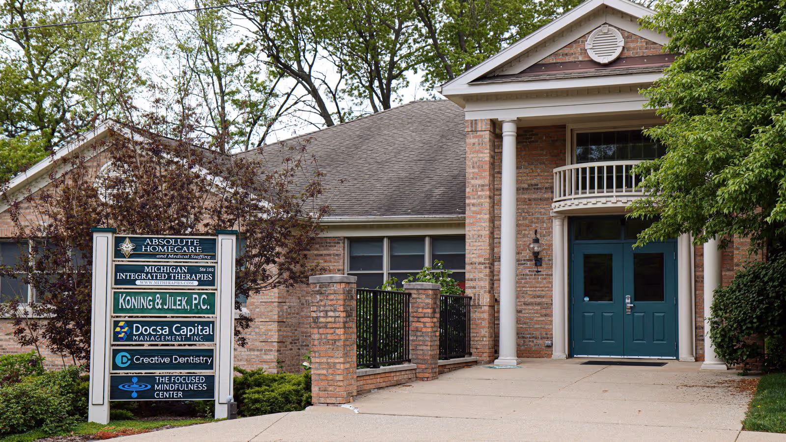 Front entrance of a brick senior living facility with teal doors and a multi-tenant signboard.