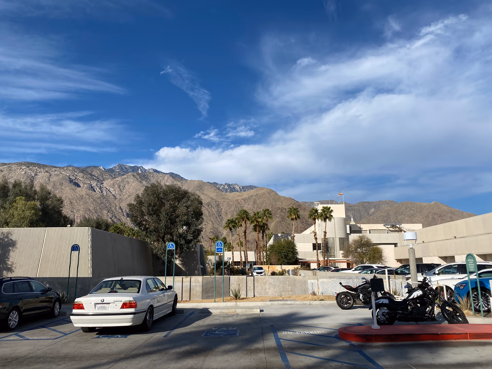 Parking lot in front of a desert hospital building with mountains in the background.