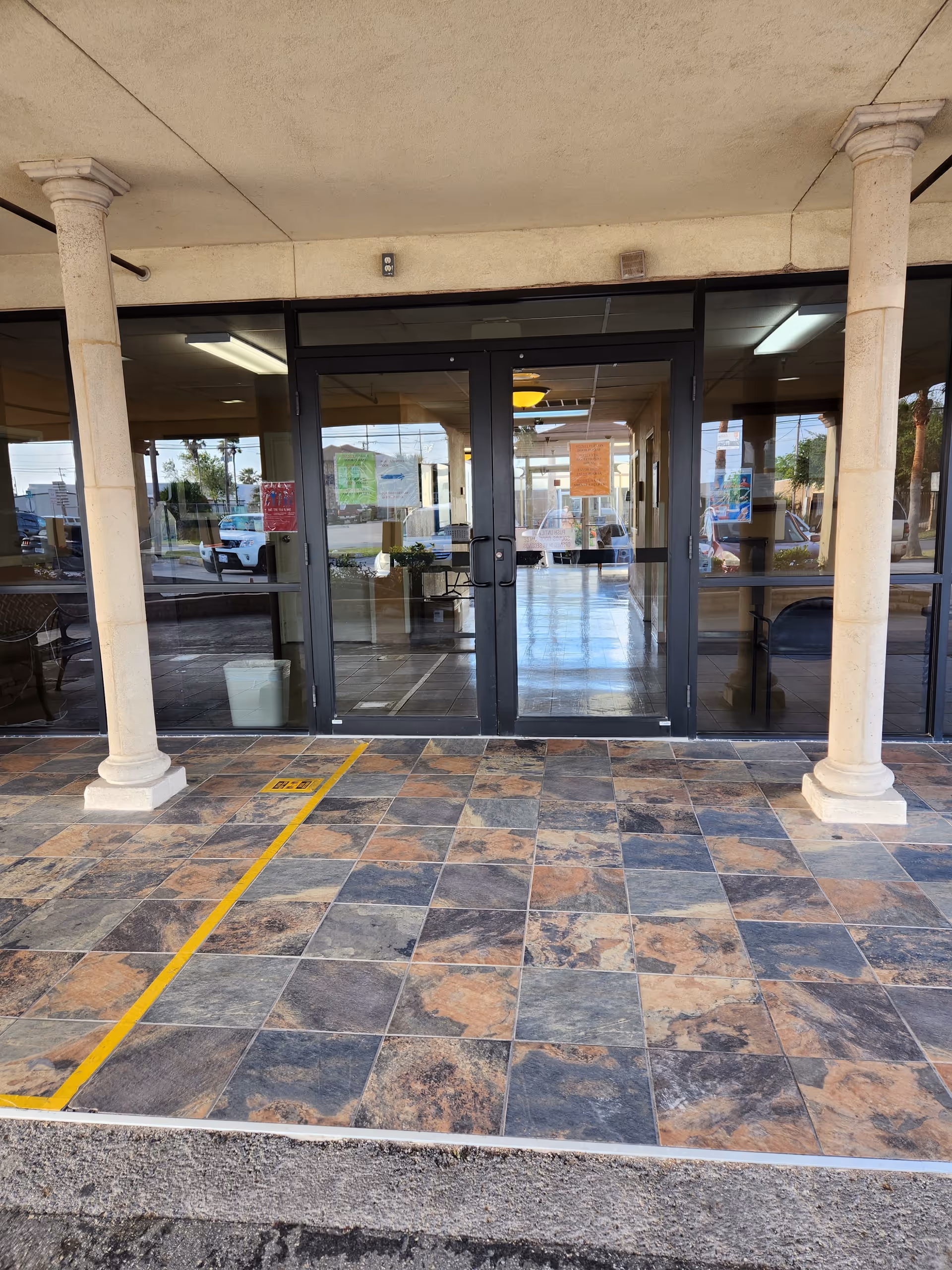 Front entrance of a building with tiled floor, glass doors, and two columns.