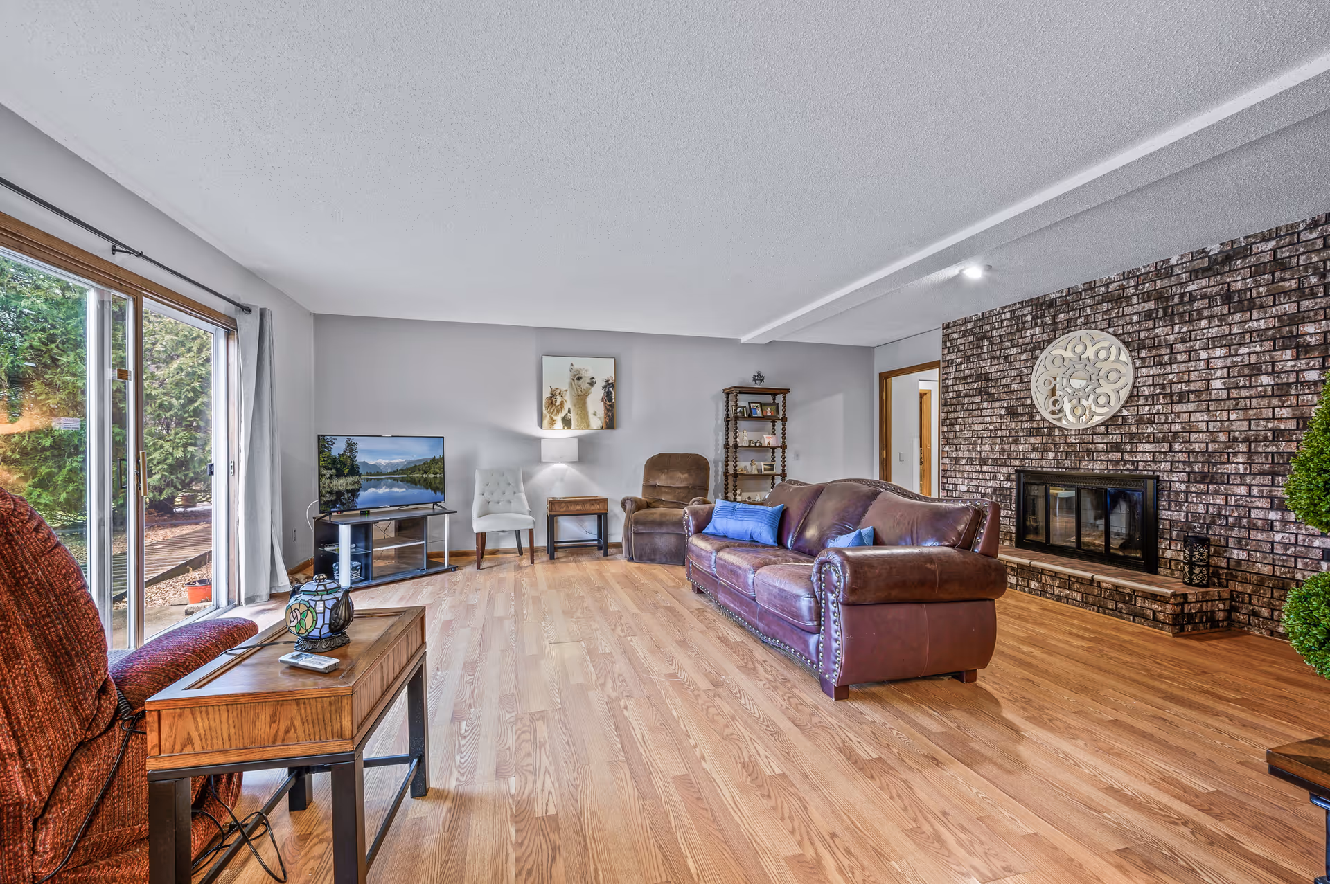 Cozy living room with brown leather sofa, brick fireplace, and sliding glass door.