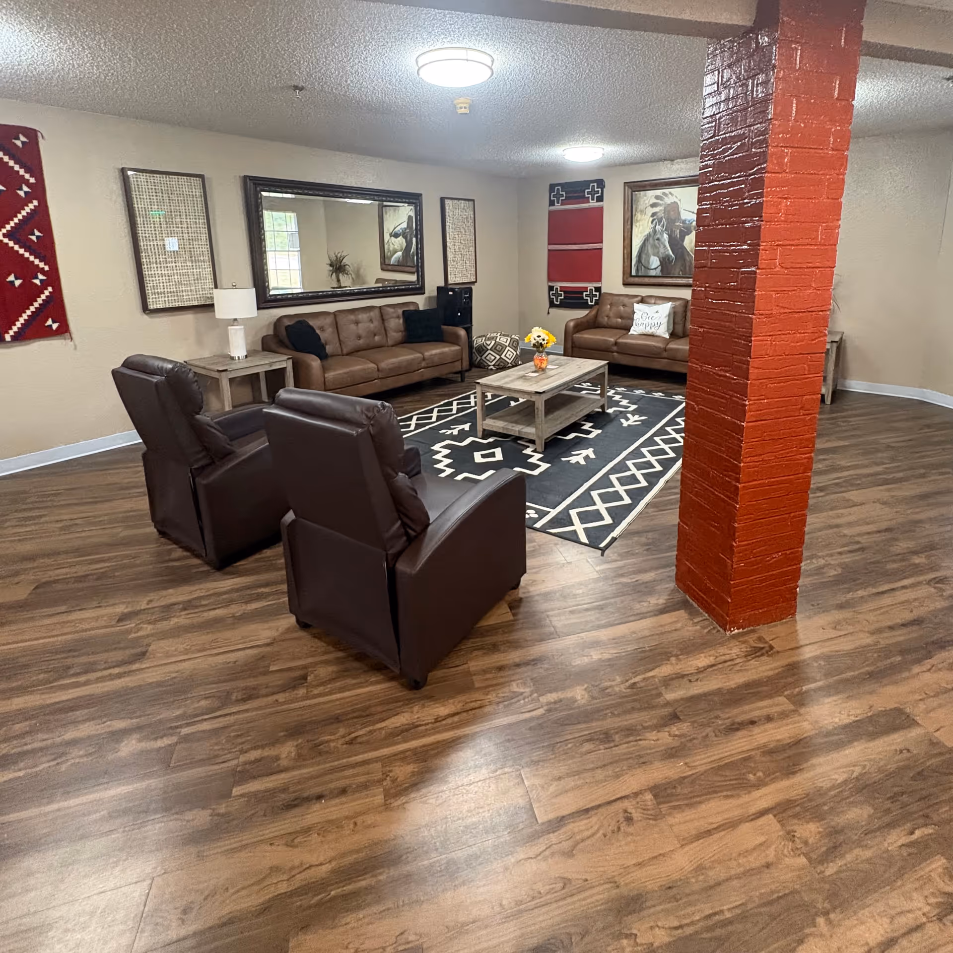 Cozy senior living lounge with leather sofas, coffee table, rug, and wall art.