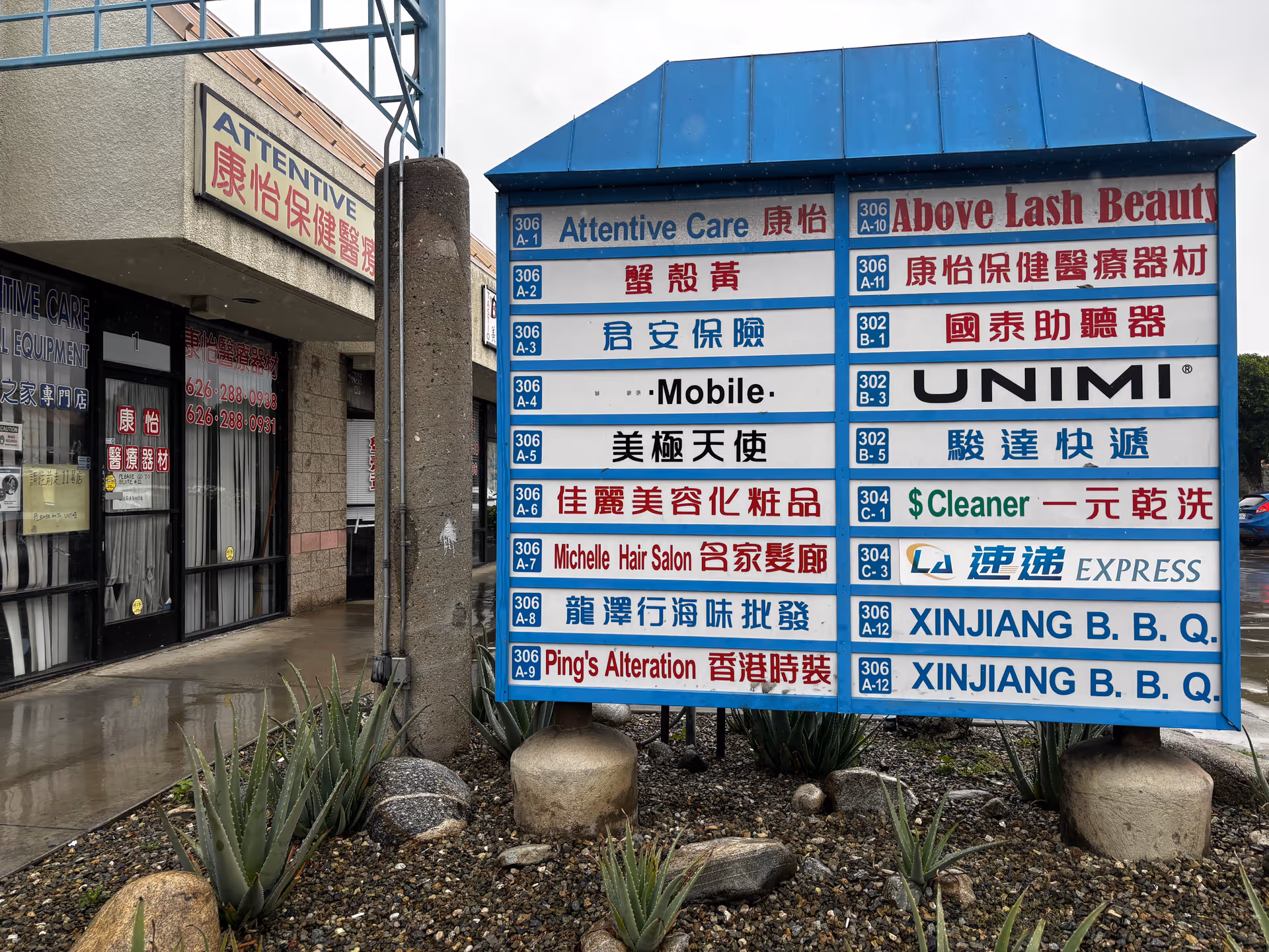 Outdoor street scene featuring a tall multi-sign board with Attentive Care and other shops