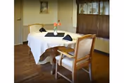 A dining table with a white tablecloth, napkins, flowers, and wooden chairs indoors.