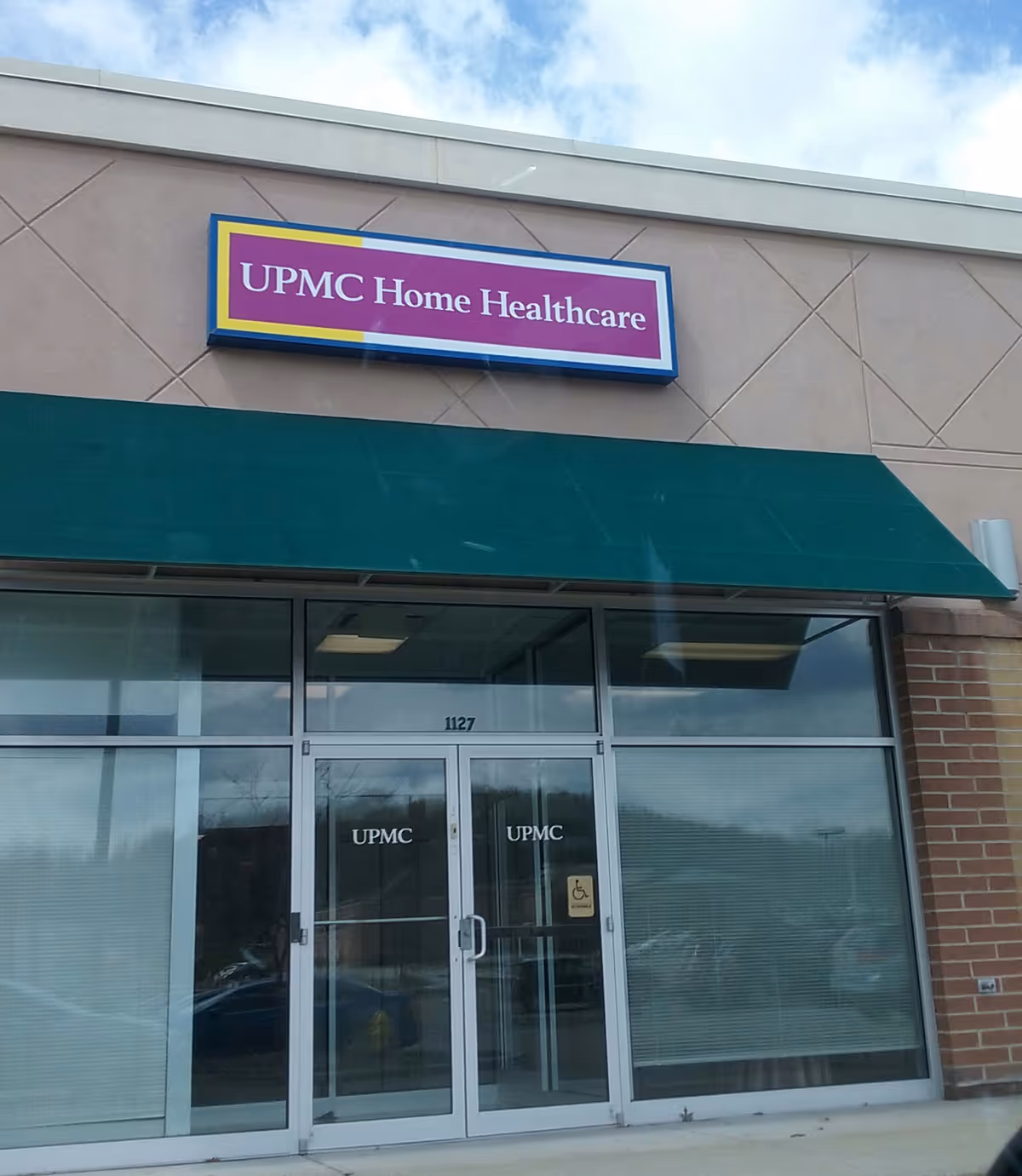Exterior view of UPMC Home Healthcare storefront with glass doors and a green awning.