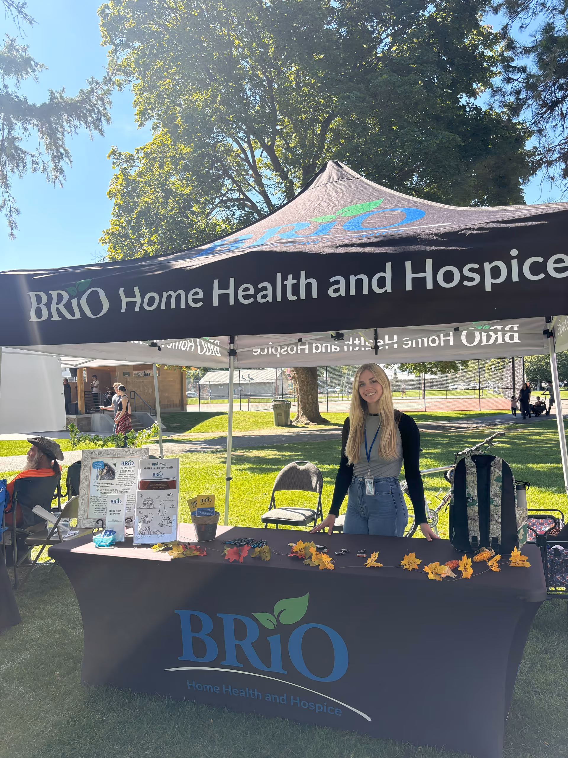 A BRiO Home Health and Hospice booth outdoors with a smiling attendant beside a table.