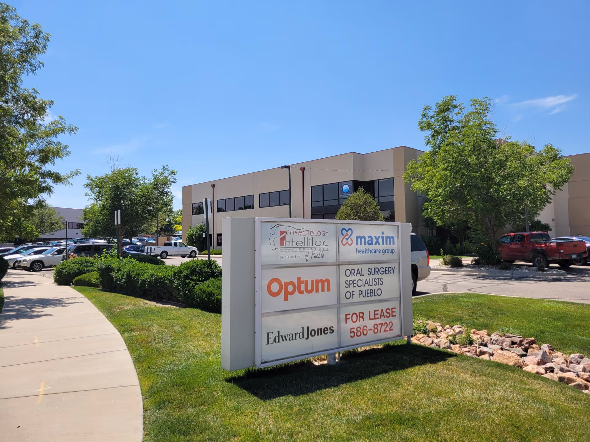 Exterior view of a beige office building with a large sign in the landscaped parking lot.