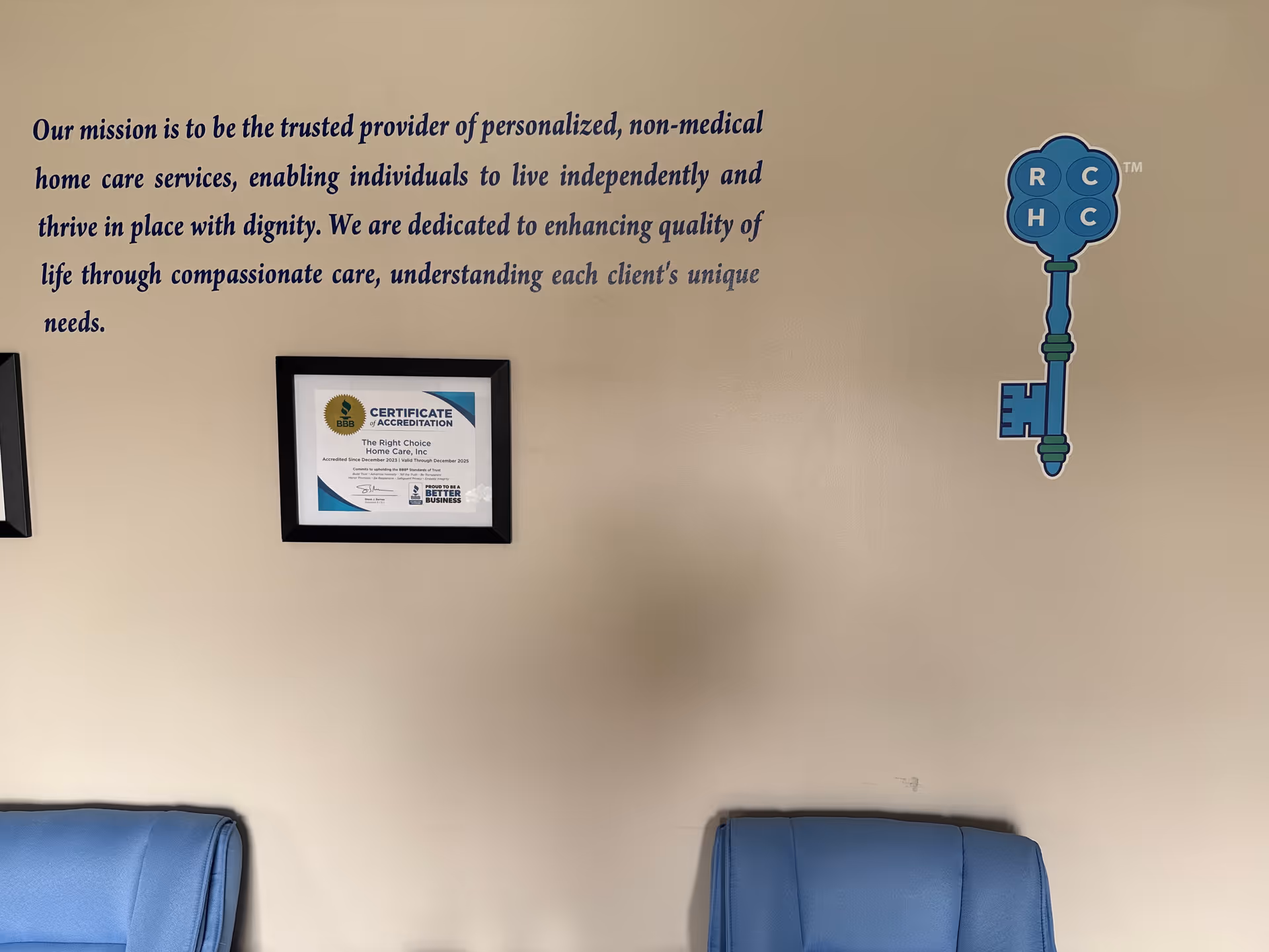 Beige wall with mission text, framed certificate, blue key graphic, and blue chairs.