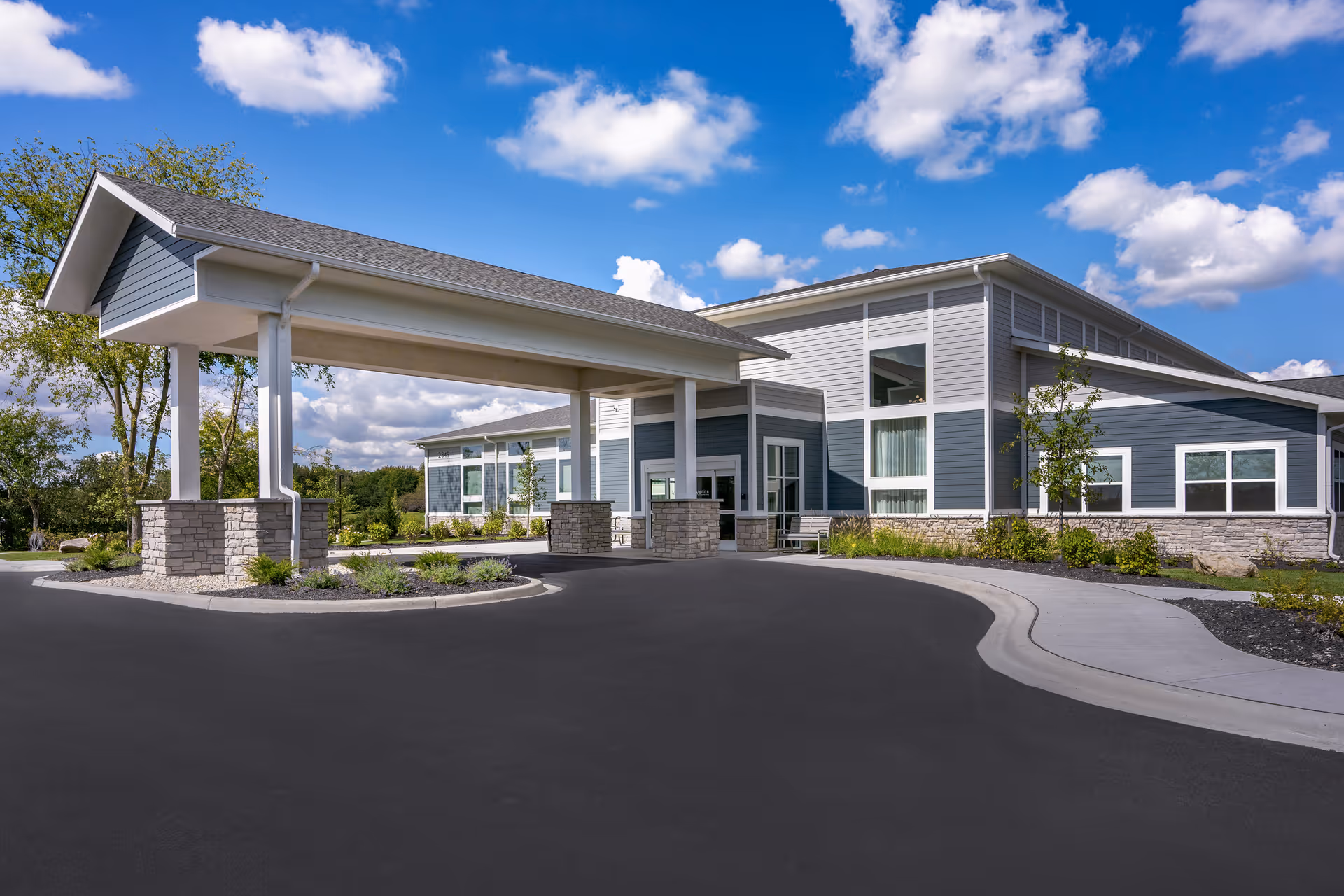 Modern senior living facility exterior with a covered entrance and circular driveway under a blue sky.