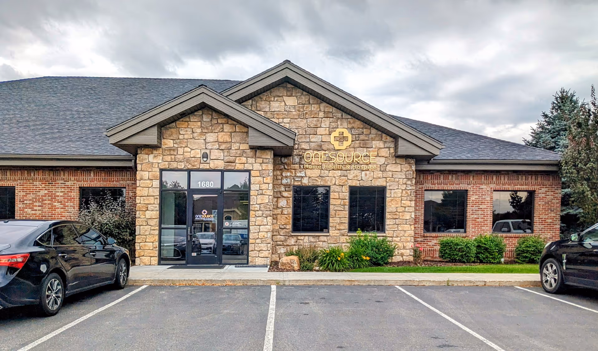 Front view of OneSource Home Health and Hospice building with stone façade and parked cars.