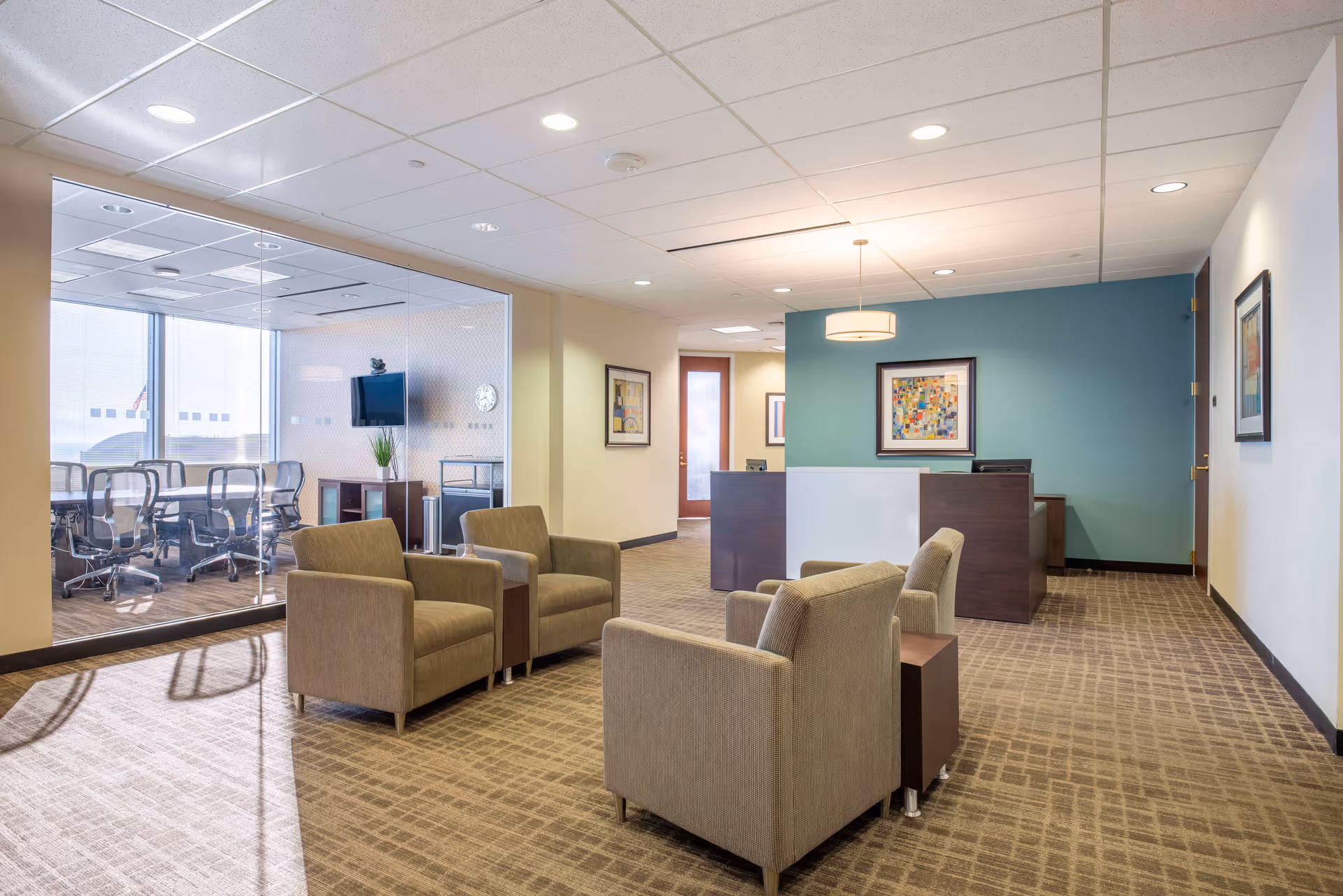 A spacious senior living lobby with beige chairs, glass partition, and a reception desk.