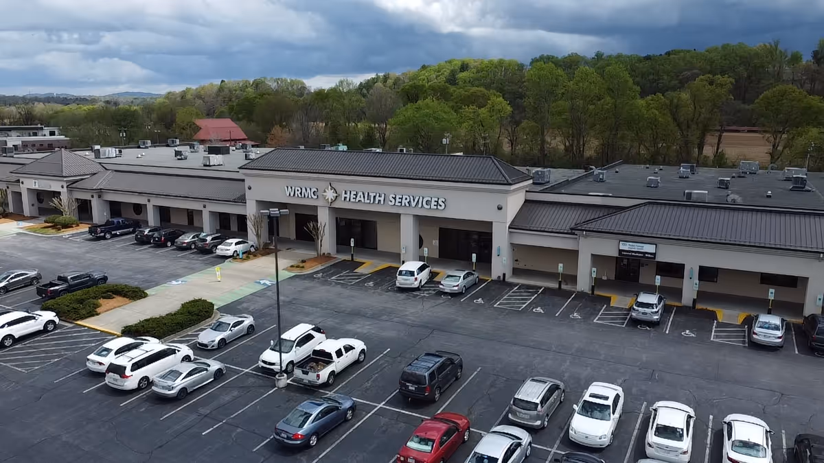 Aerial view of a medical facility with parking lot and surrounding trees.