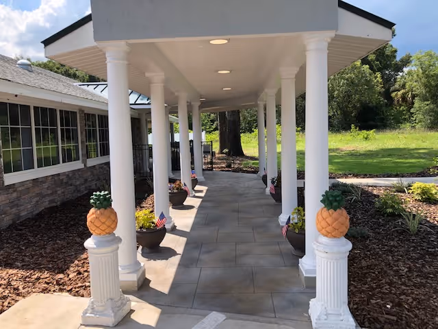 Covered walkway with white columns leads to a facility entrance and landscaping.