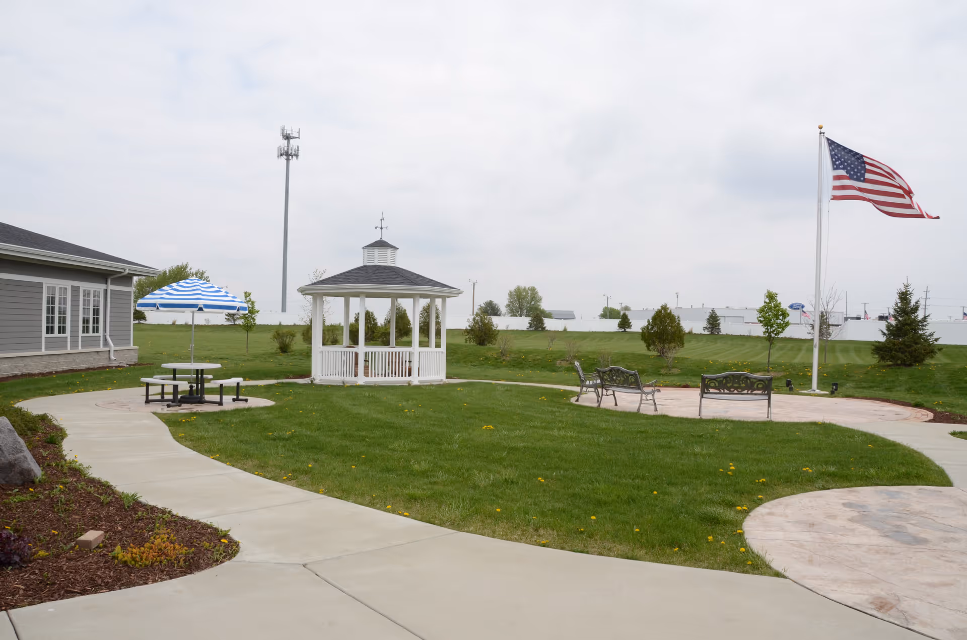 Open outdoor courtyard with gazebo, benches, umbrella-shaded table, and flagpole.