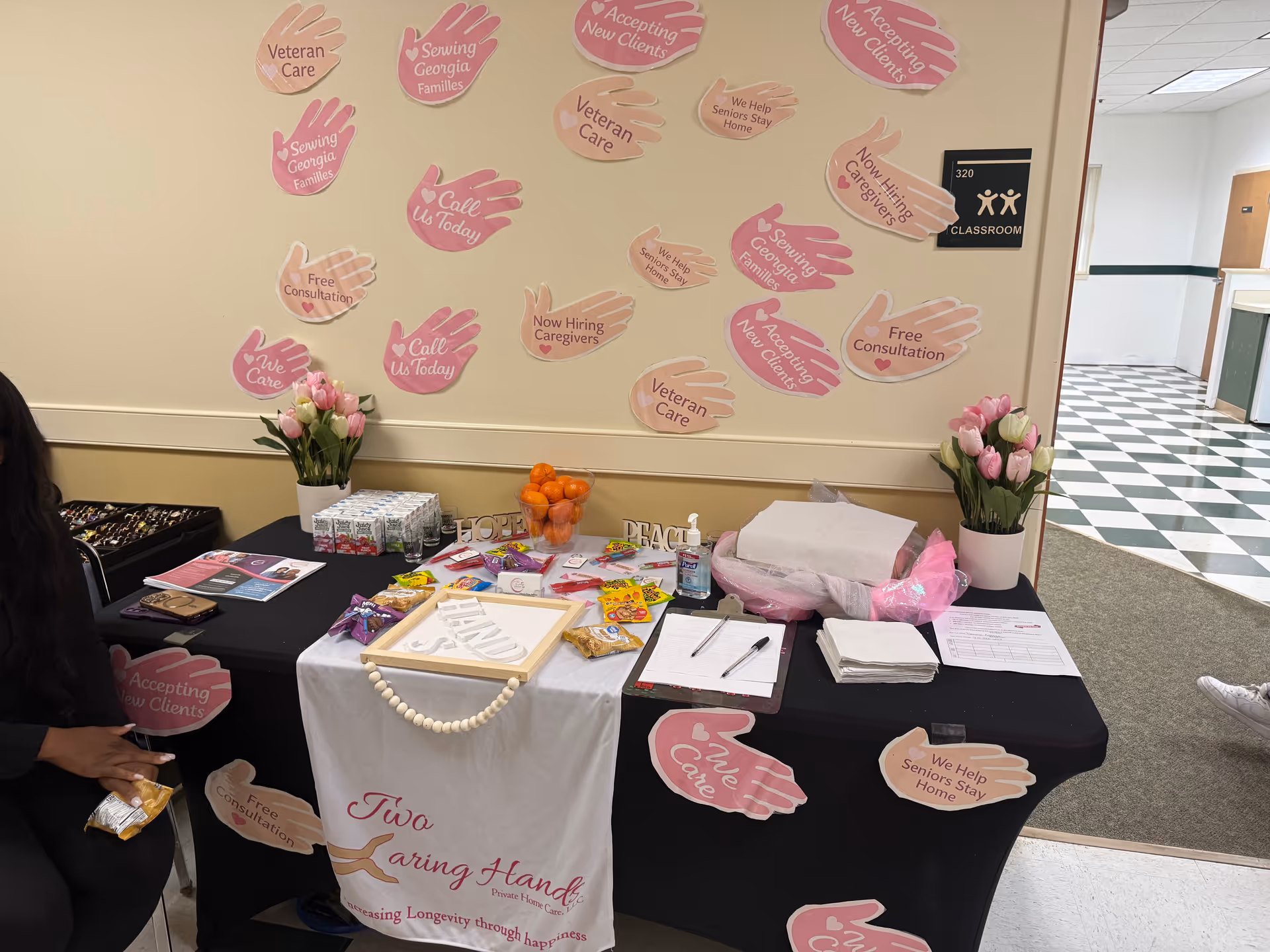Information table with pink hand signs, flowers, and brochures inside a private home care facility.