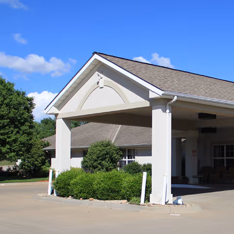 Exterior view of Vintage Park at Wamego entrance with covered driveway, columns, and shrubs.