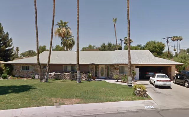 Single-story senior living building with a manicured lawn, palm trees, and parked cars in driveway.