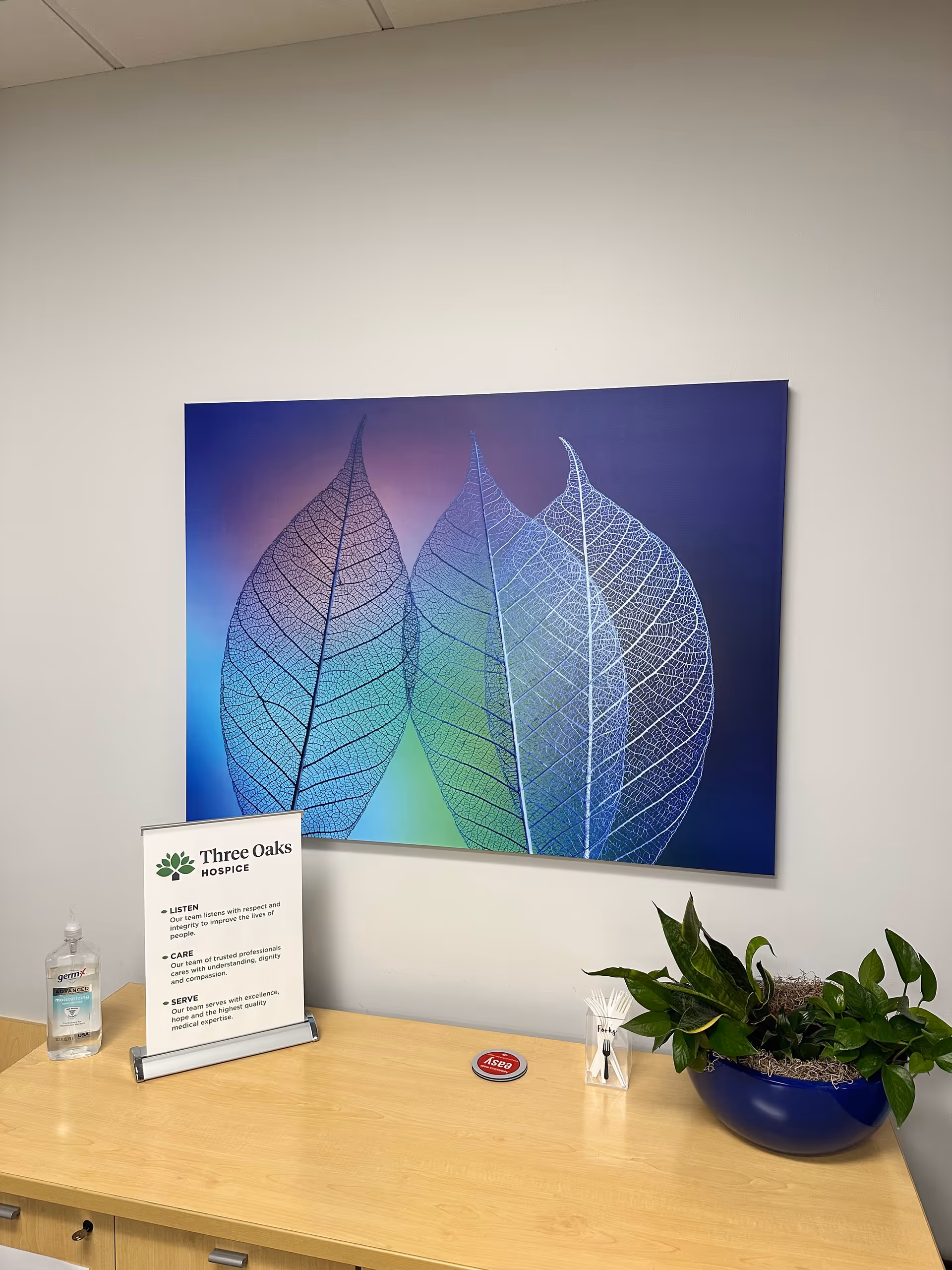 Reception desk area with Three Oaks Hospice sign, hand sanitizer, and leaf artwork.