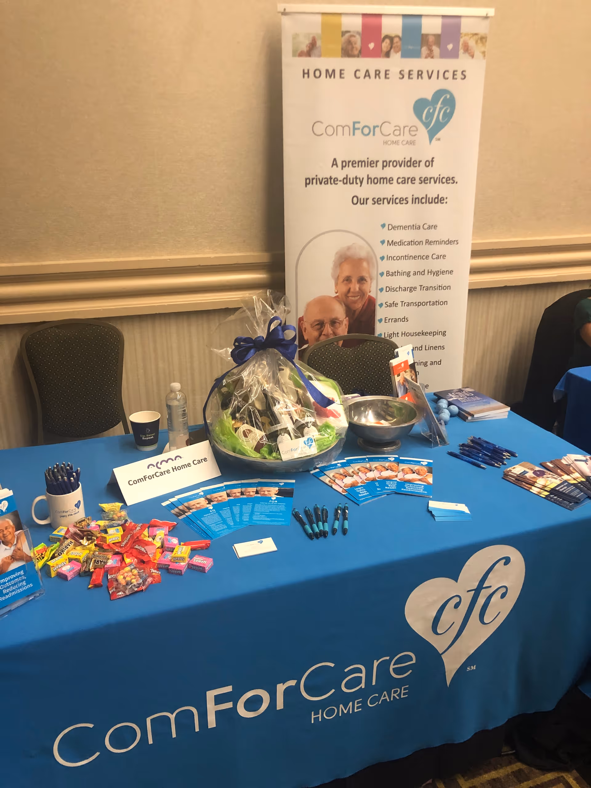 Promotional booth for ComForCare Home Care Services with banner, table, basket, and brochures.