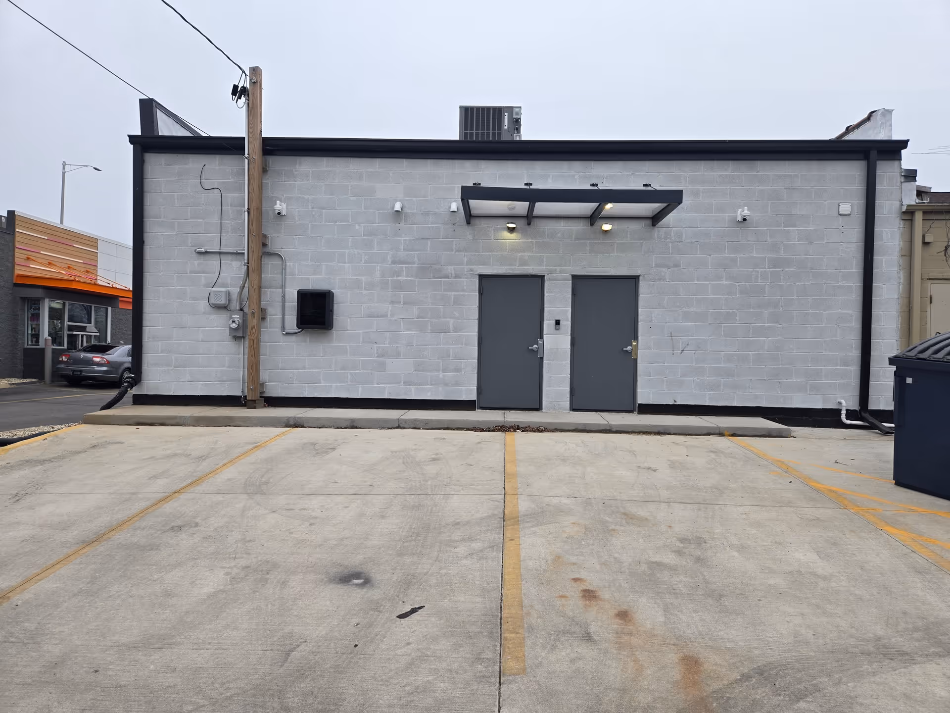 Gray concrete building exterior with two gray doors, a small canopy, and an empty parking lot.