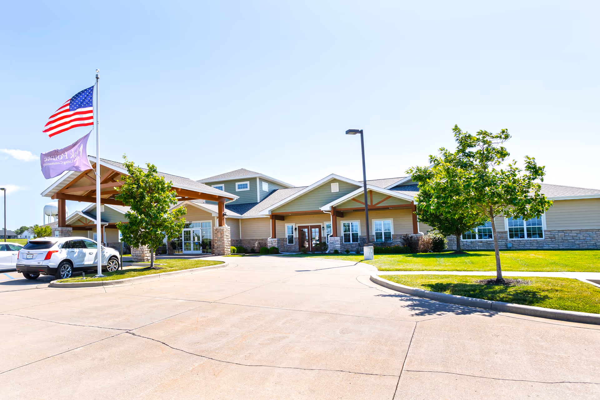 Oak Pointe of Maryville exterior with flag, entrance, a car, and trees.