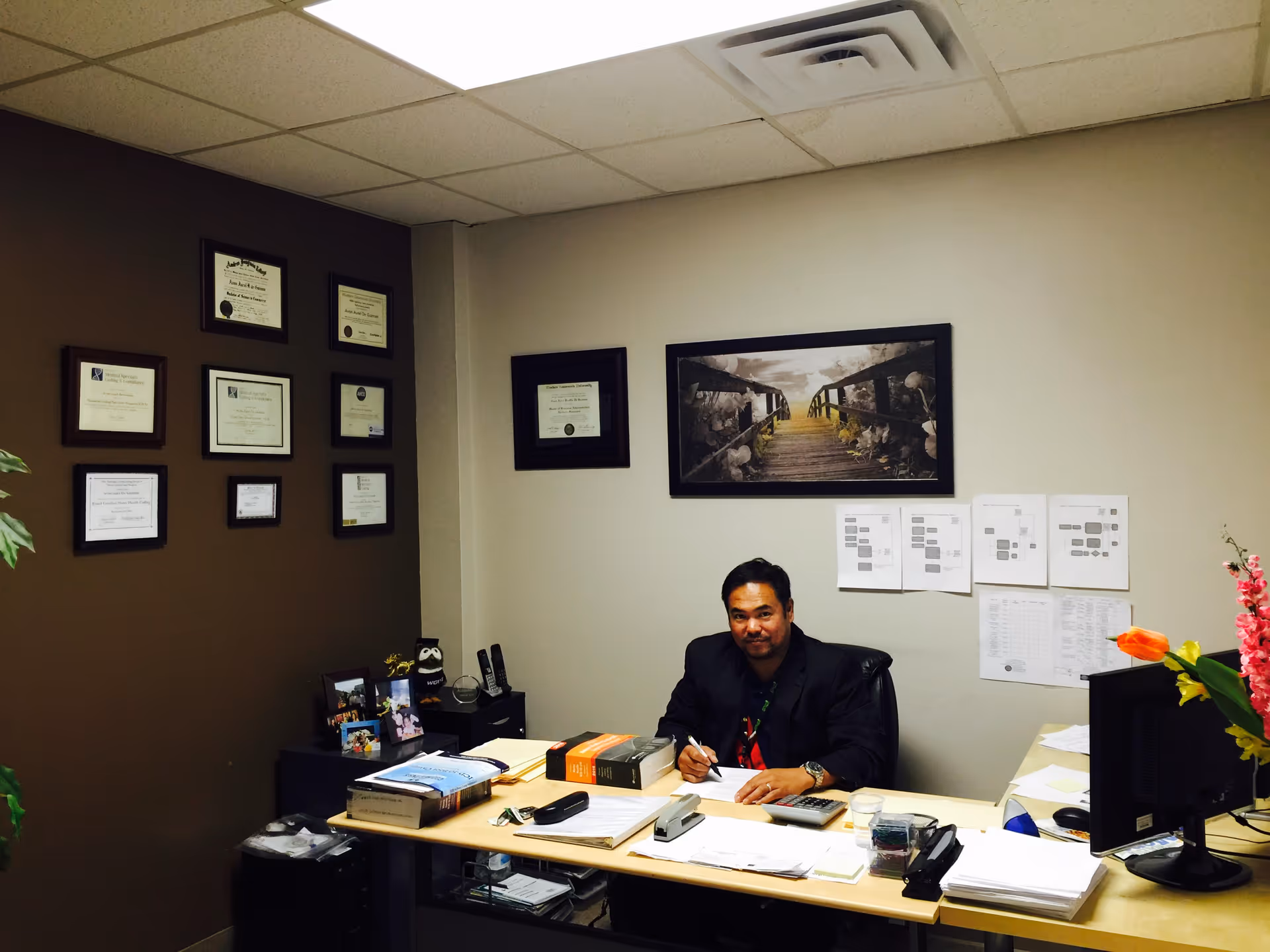 A man sits at a desk in a professional office, walls lined with certificates.