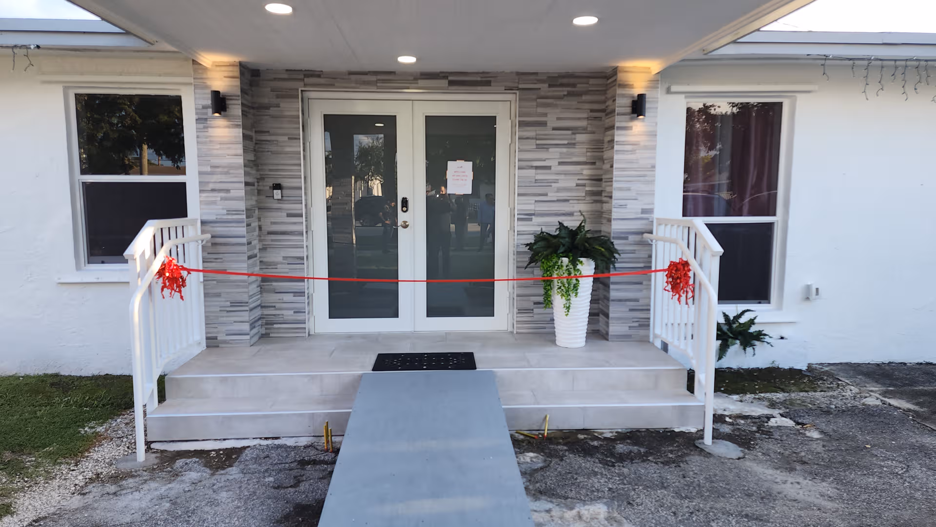Front entrance of Ave Fenix ALF LLC with double doors, ramp, and potted plants.