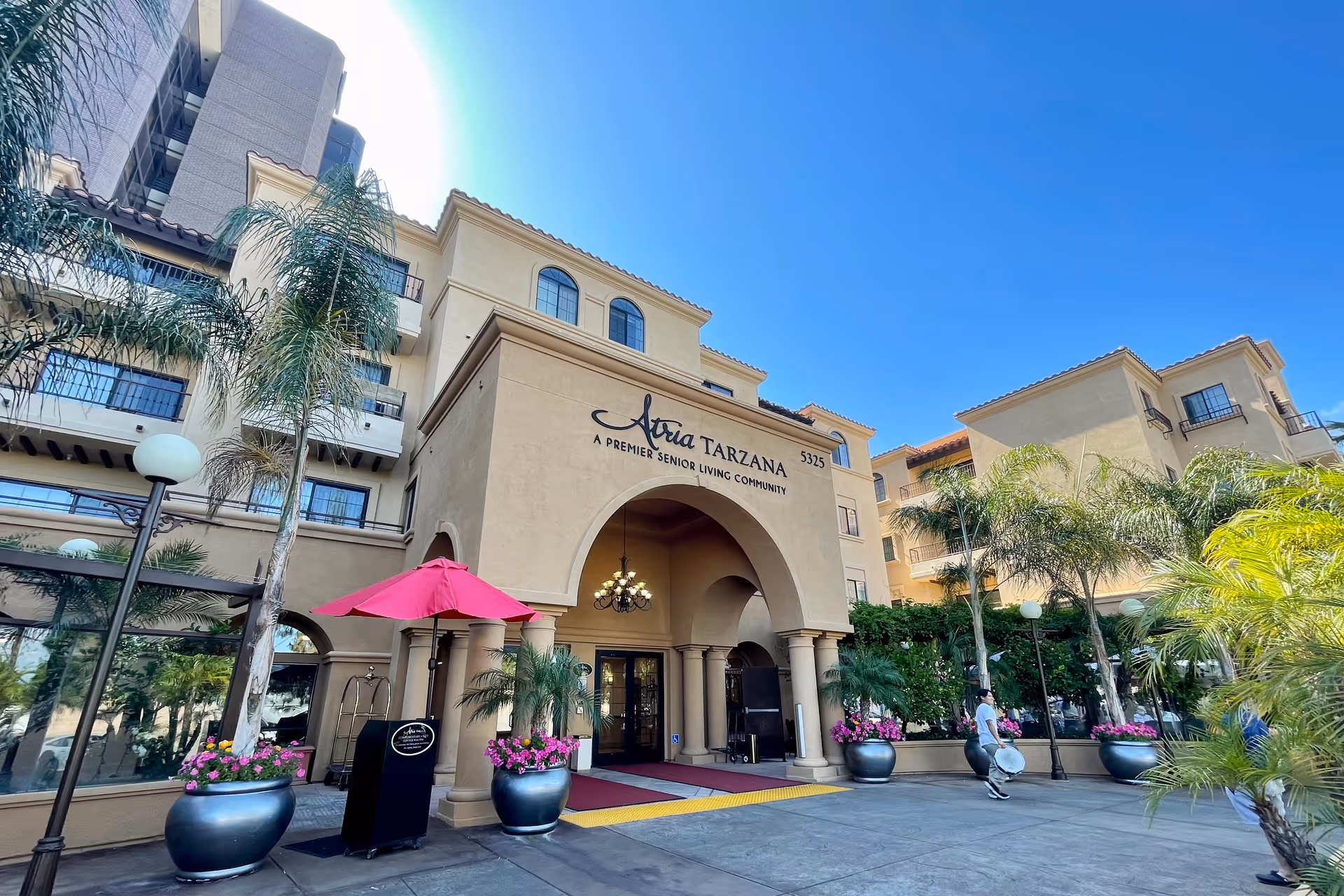 Exterior view of Atria Tarzana entrance with arches, palm trees, and potted plants.