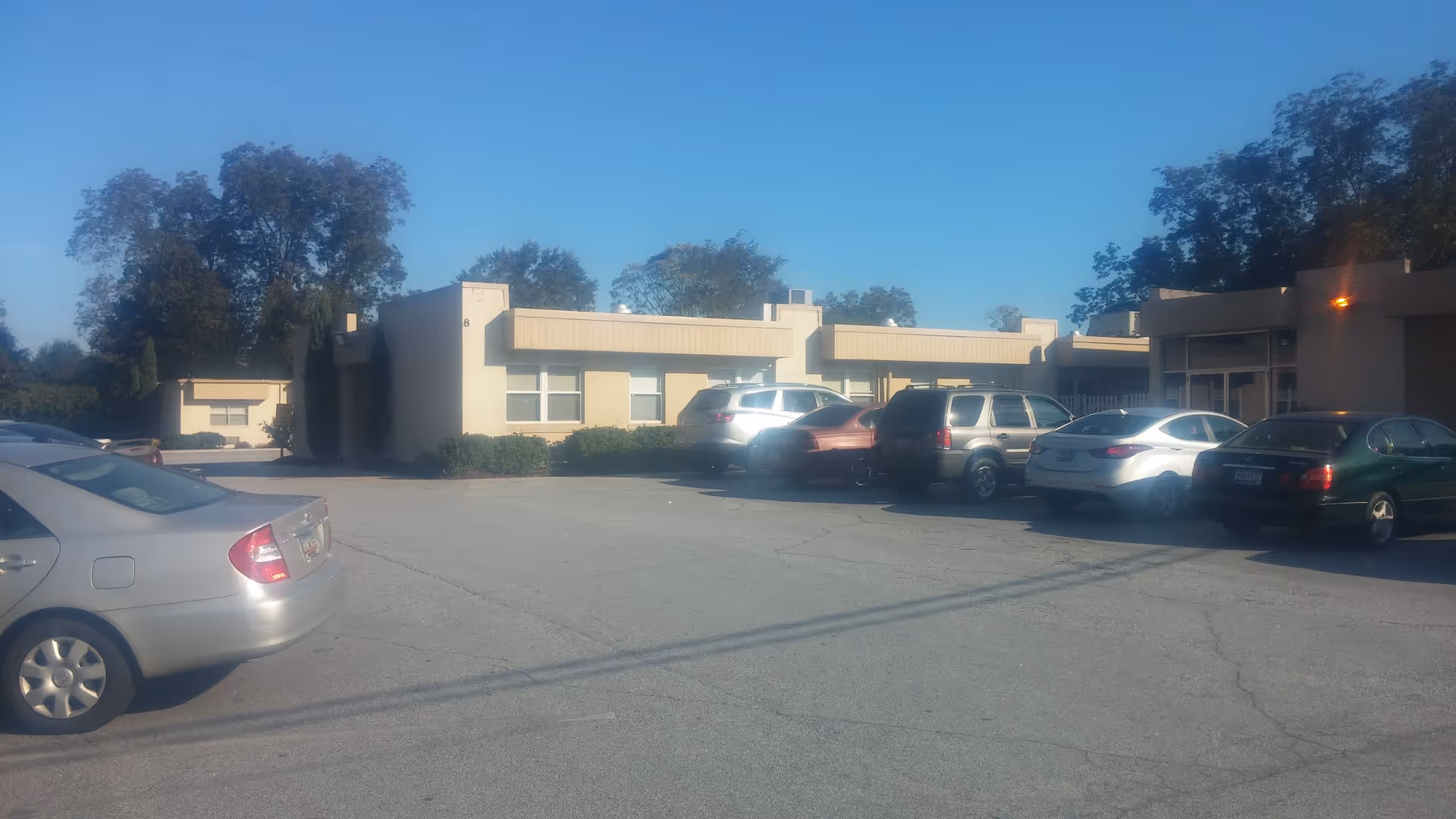 Exterior view of a beige senior living building with a parking lot and trees.