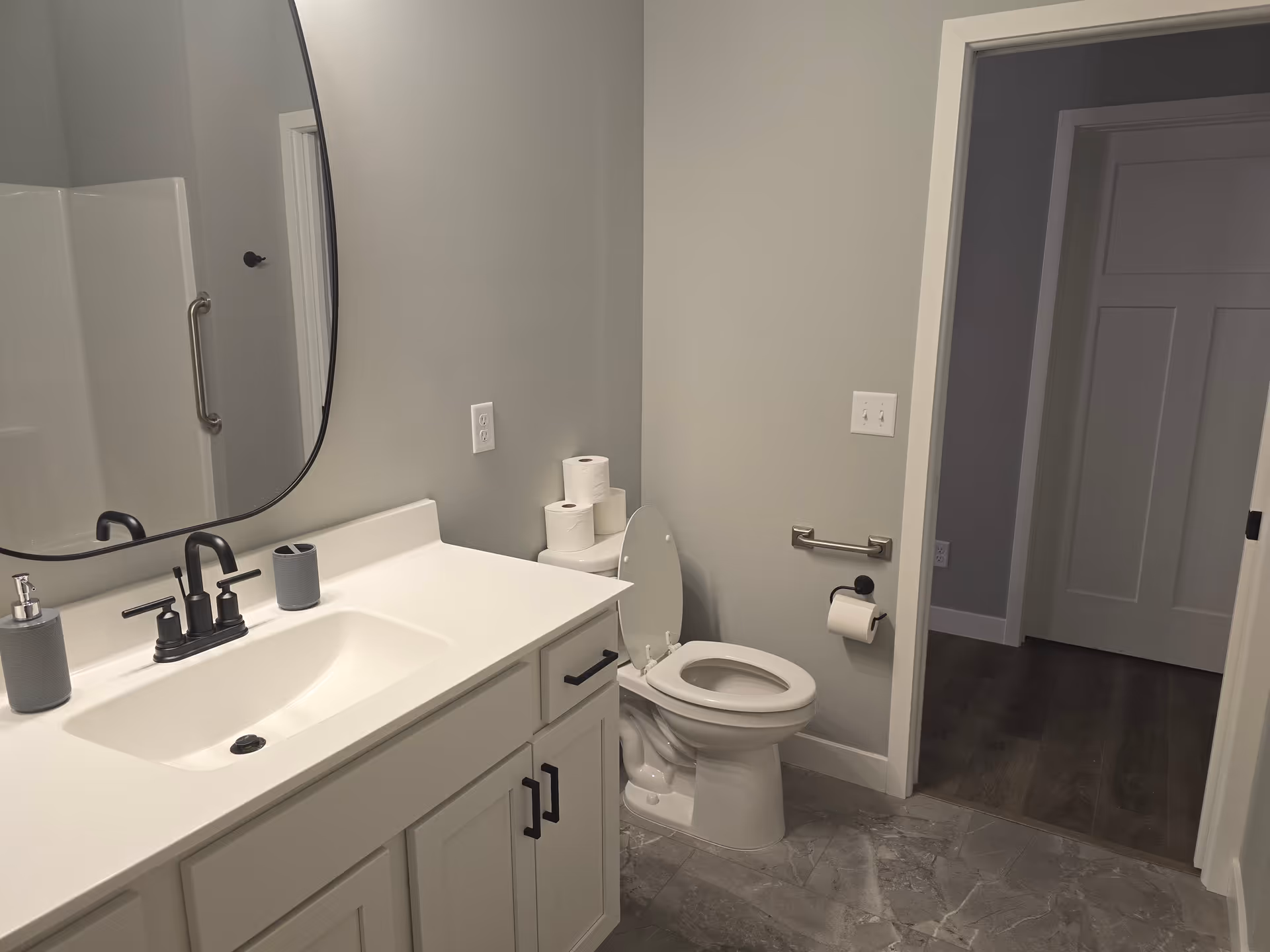Modern senior living facility bathroom with sink, large mirror, toilet, and accessibility grab bar.