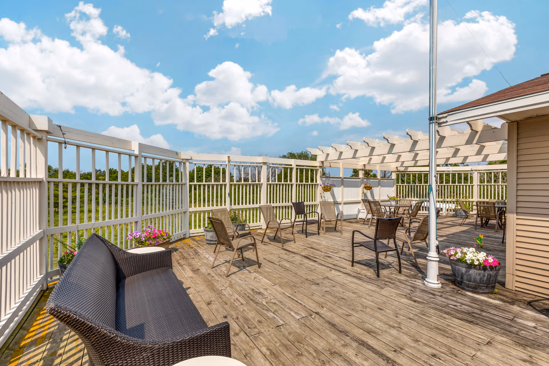 Rooftop wooden terrace with seating, planters, and white pergola under a blue sky.