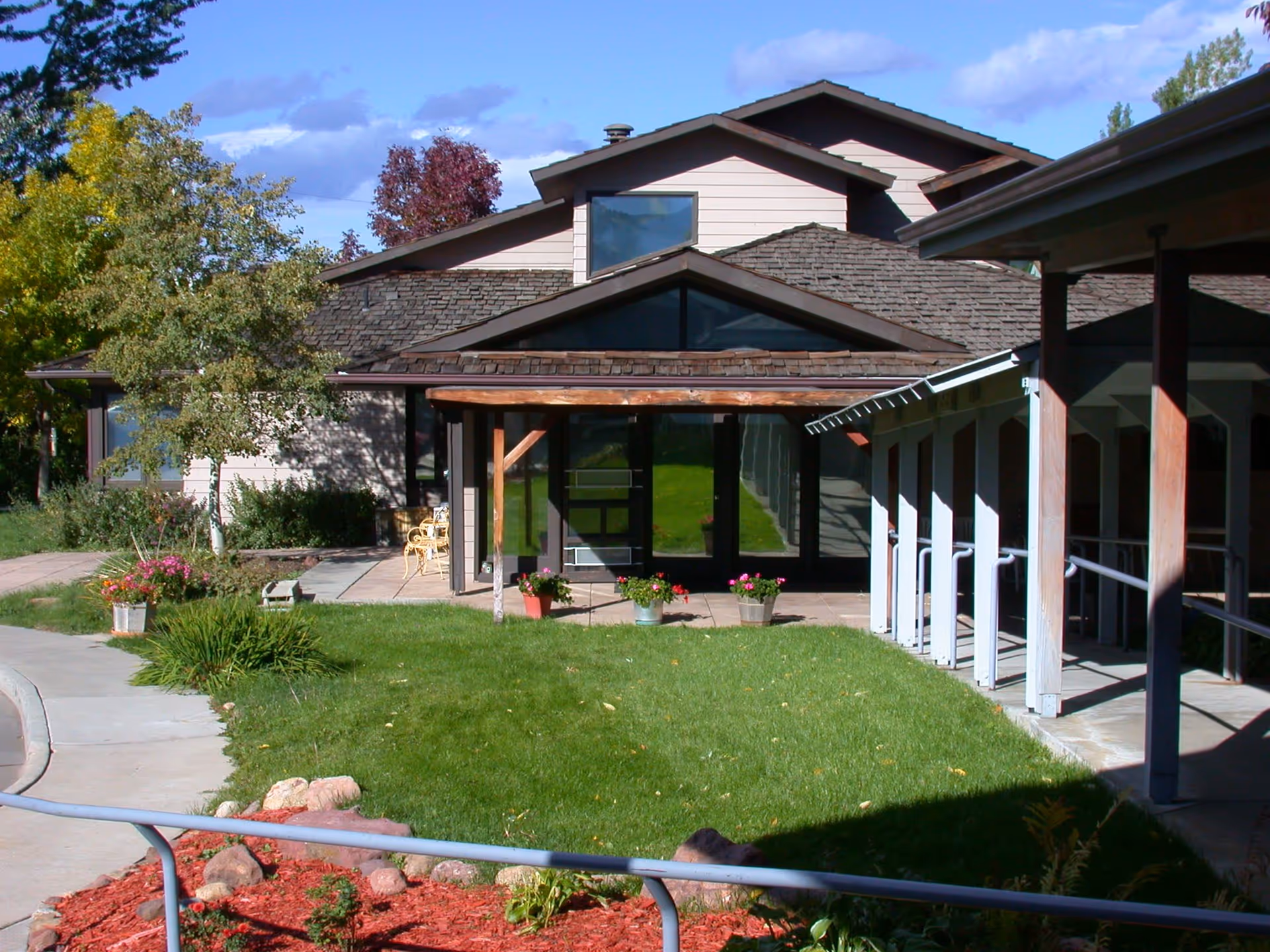 Front entrance of a single-story building with a covered porch, walkway, lawn, and potted flowers.