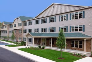 Three-story beige senior living building with green awnings and manicured lawn.