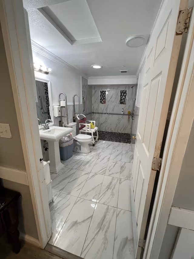 Accessible bathroom with sink, toilet, grab bars, and marble-tile flooring.