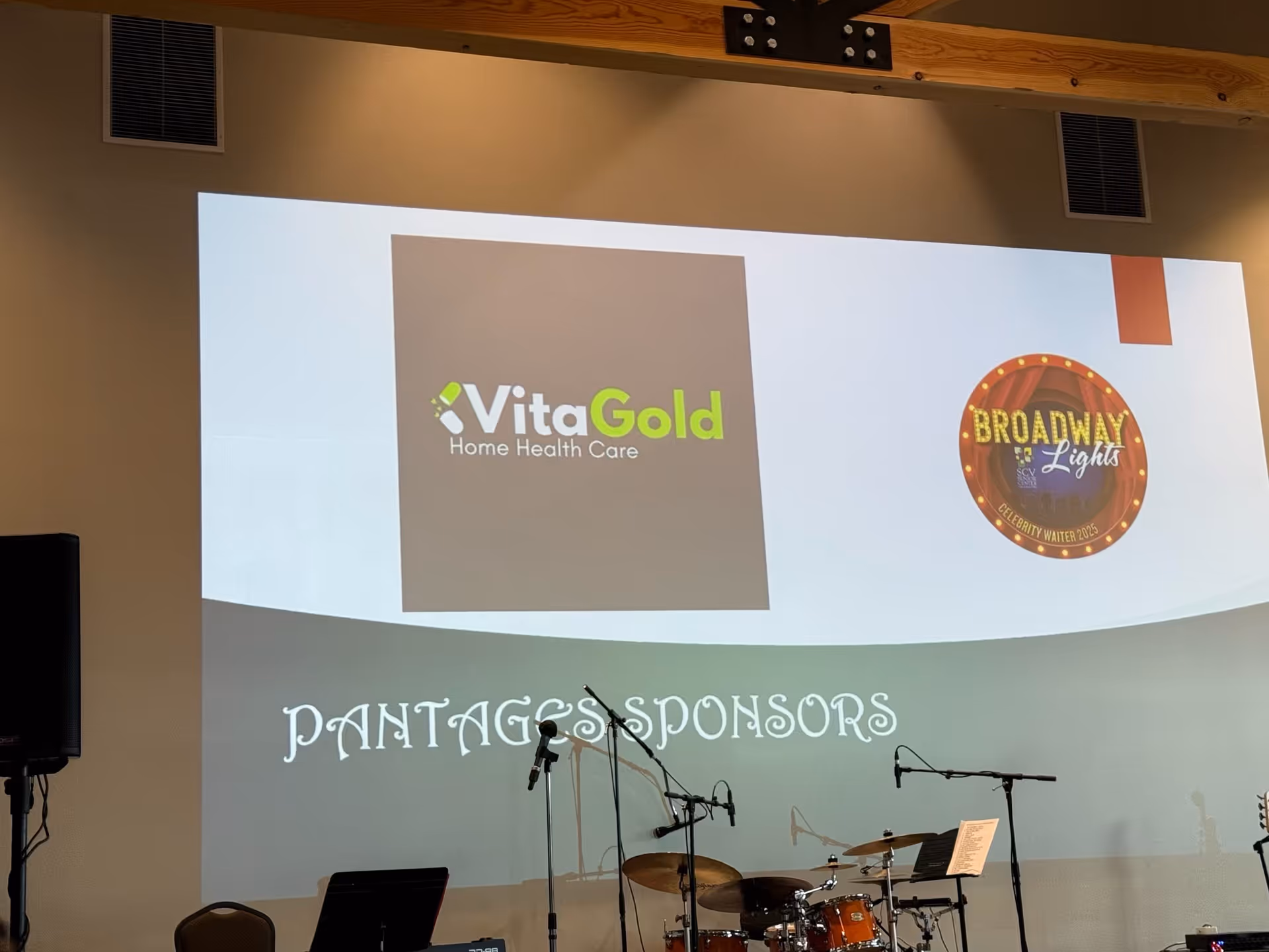 Indoor stage with a large VitaGold Home Health Care projection screen.