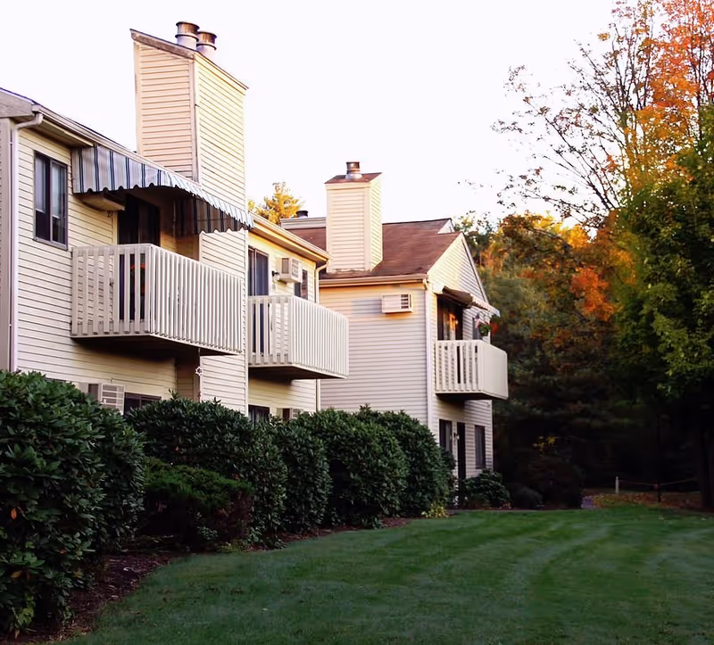 Exterior view of a multi-unit senior living building with balconies, hedges, and autumn trees.