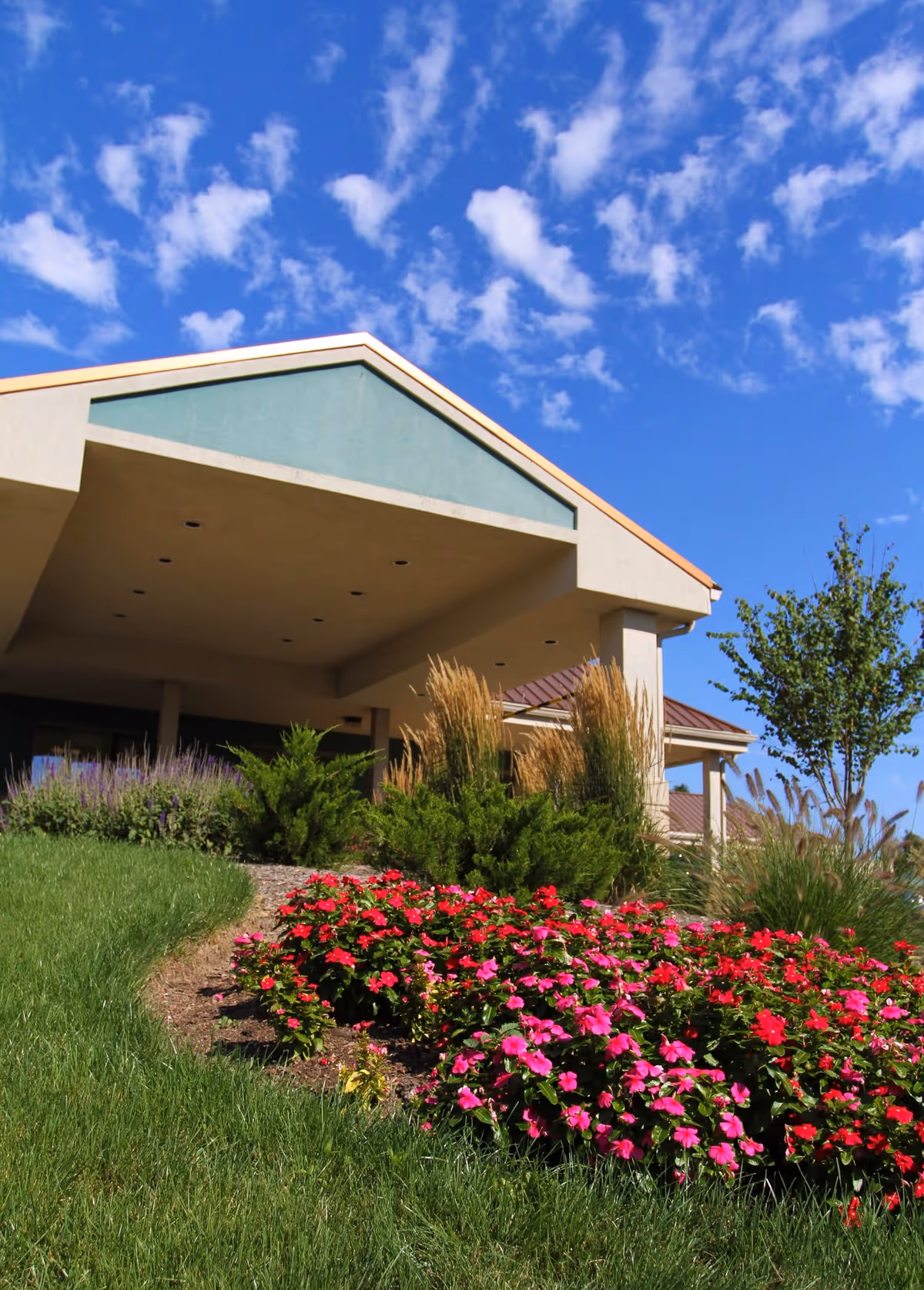 Exterior view of a senior living facility with landscaped flower beds and a blue sky.